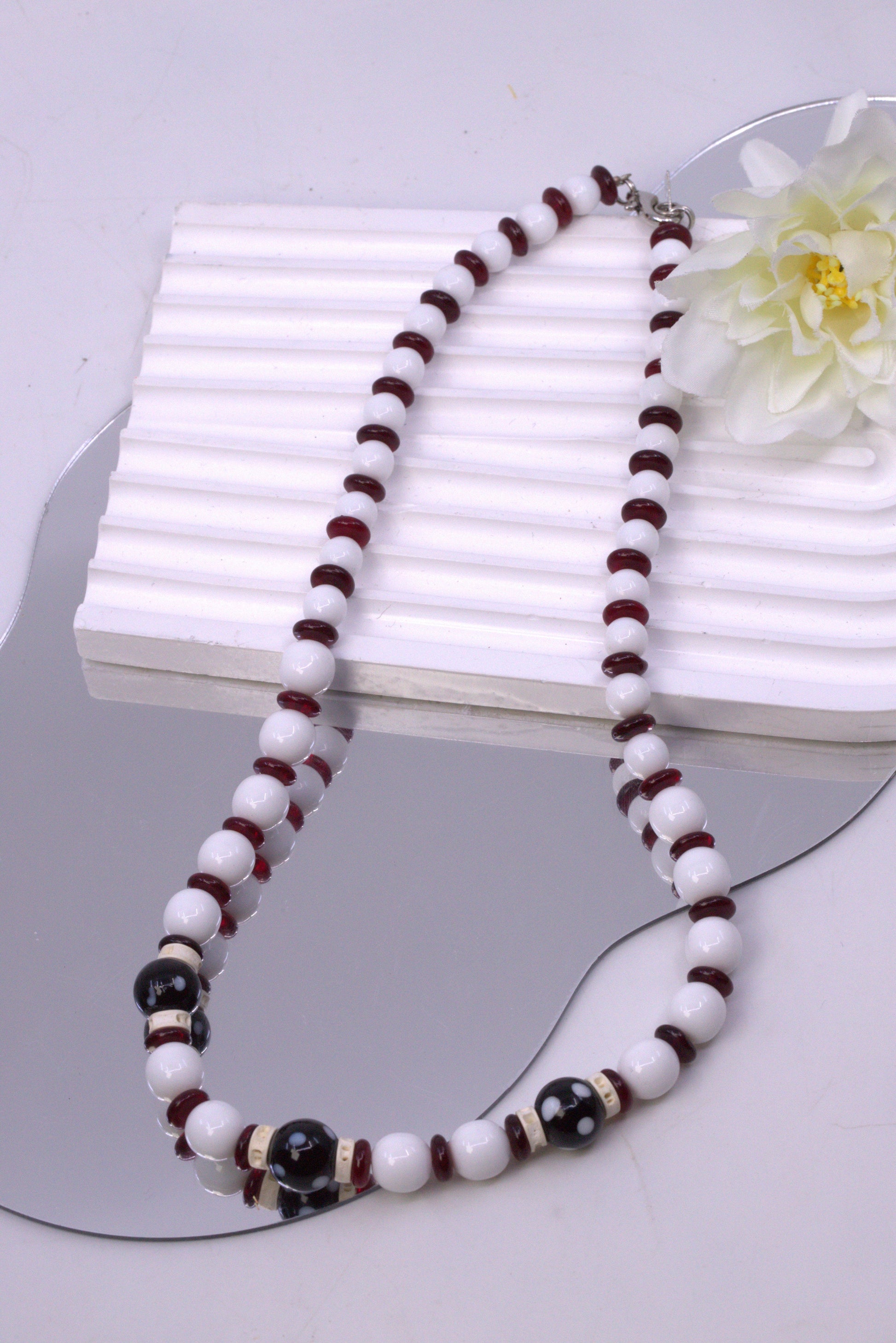 Necklace with white and brown beads on a white surface with a flower.