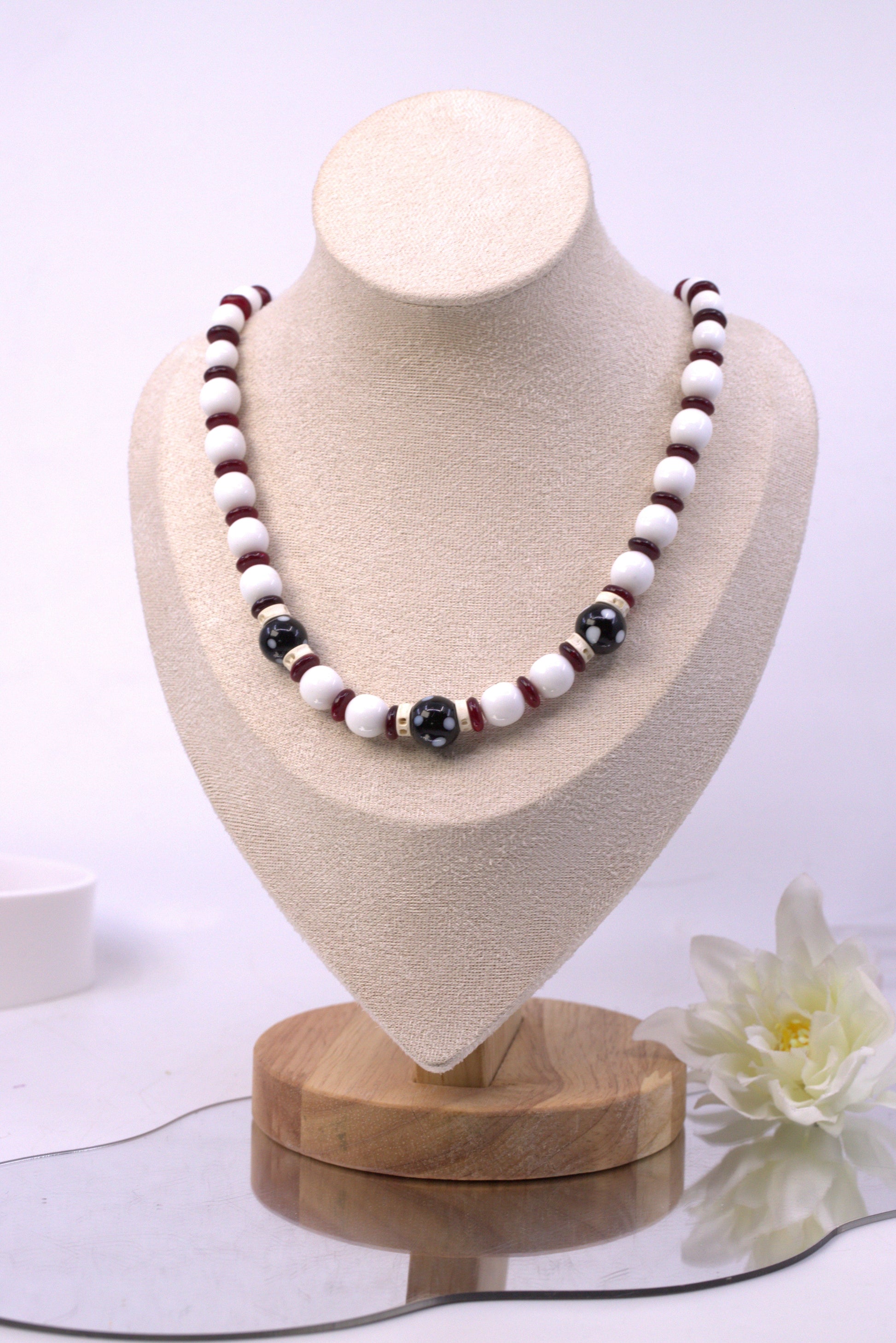 Necklace with black, white, and red beads on a beige bust with a white background