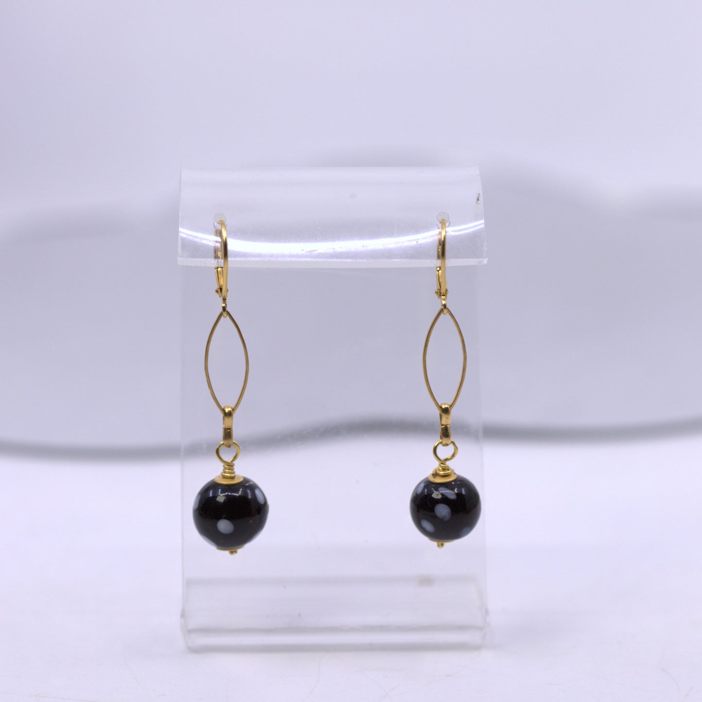 Black beaded earrings with gold hooks on a clear stand against a white background. evil eye earrings