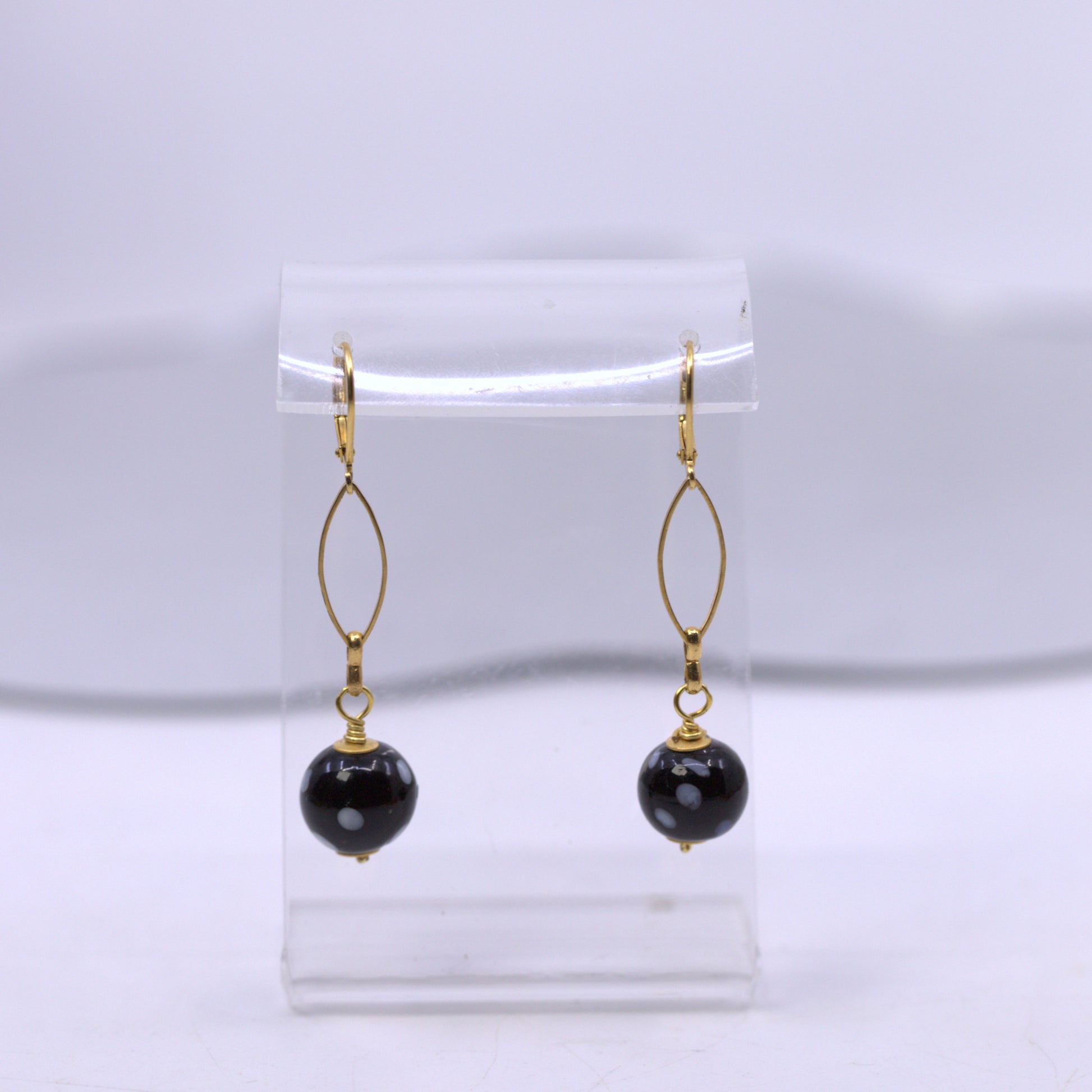 Black beaded earrings with gold hooks on a clear stand against a white background. evil eye earrings
