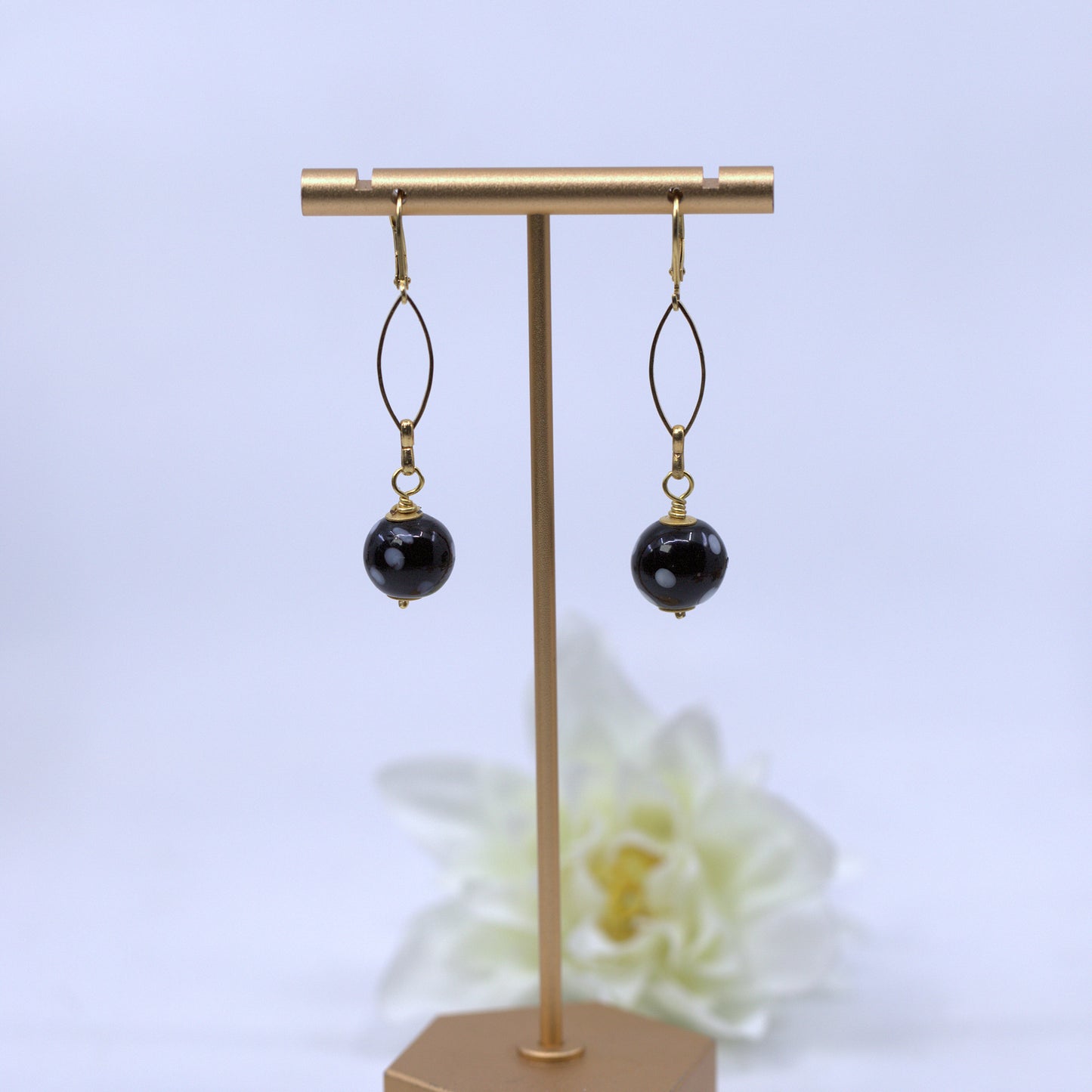 Black beaded earrings on a gold earring stand with a white flower in the background. Evil eye earrings