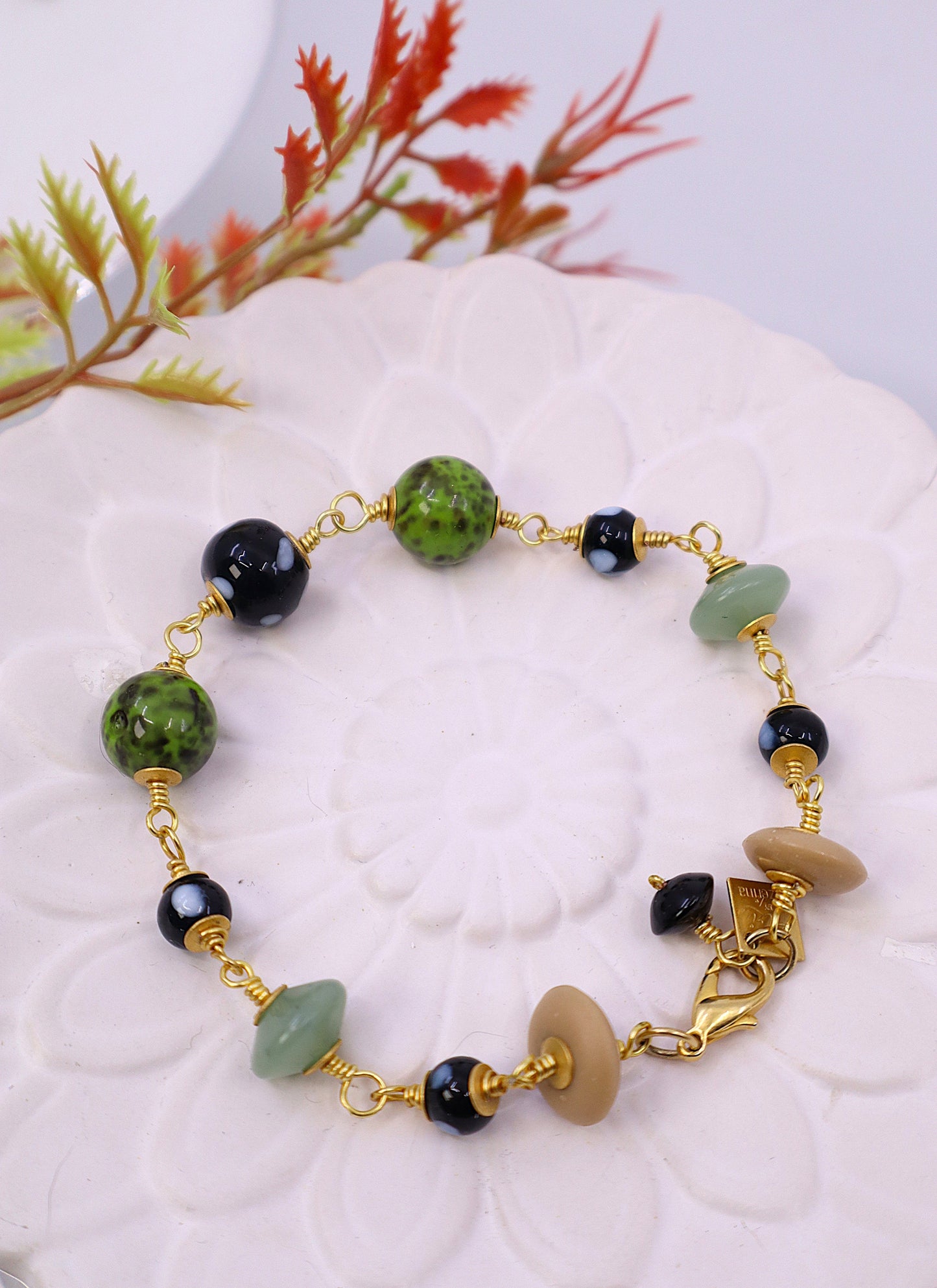 Bracelet with green, black, and gold beads on a white surface with decorative elements.