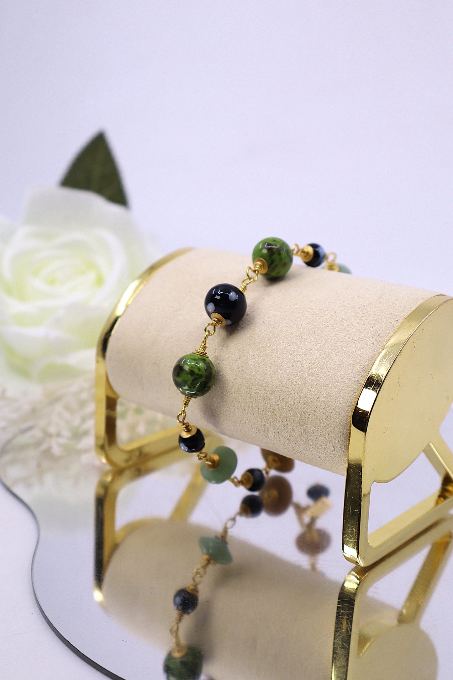 Beaded bracelet on a gold stand with a white flower in the background