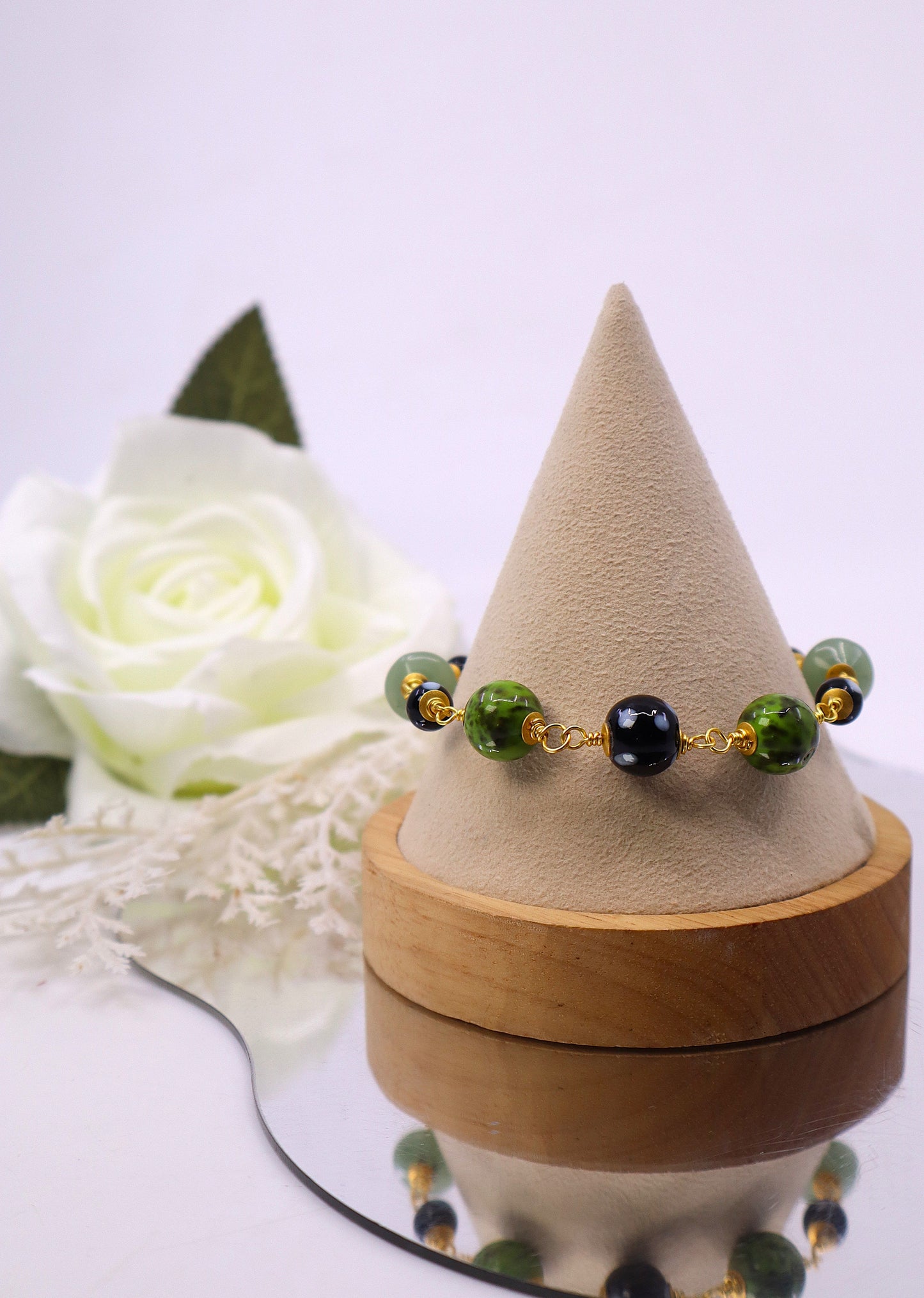 Bracelet with green and black beads on a wooden stand with a white rose in the background