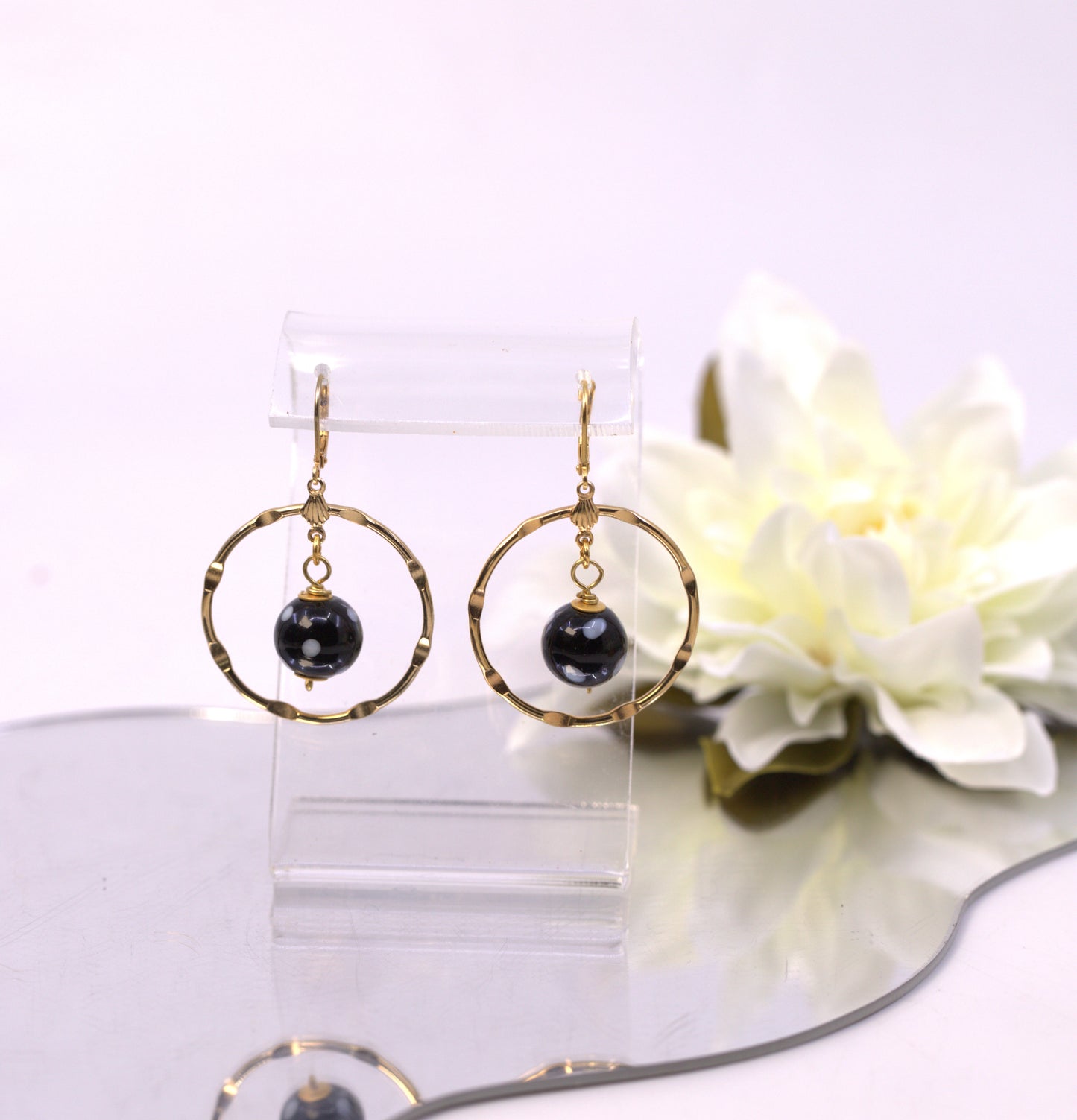 Gold hoop earrings with black beads on a clear stand with a white flower in the background