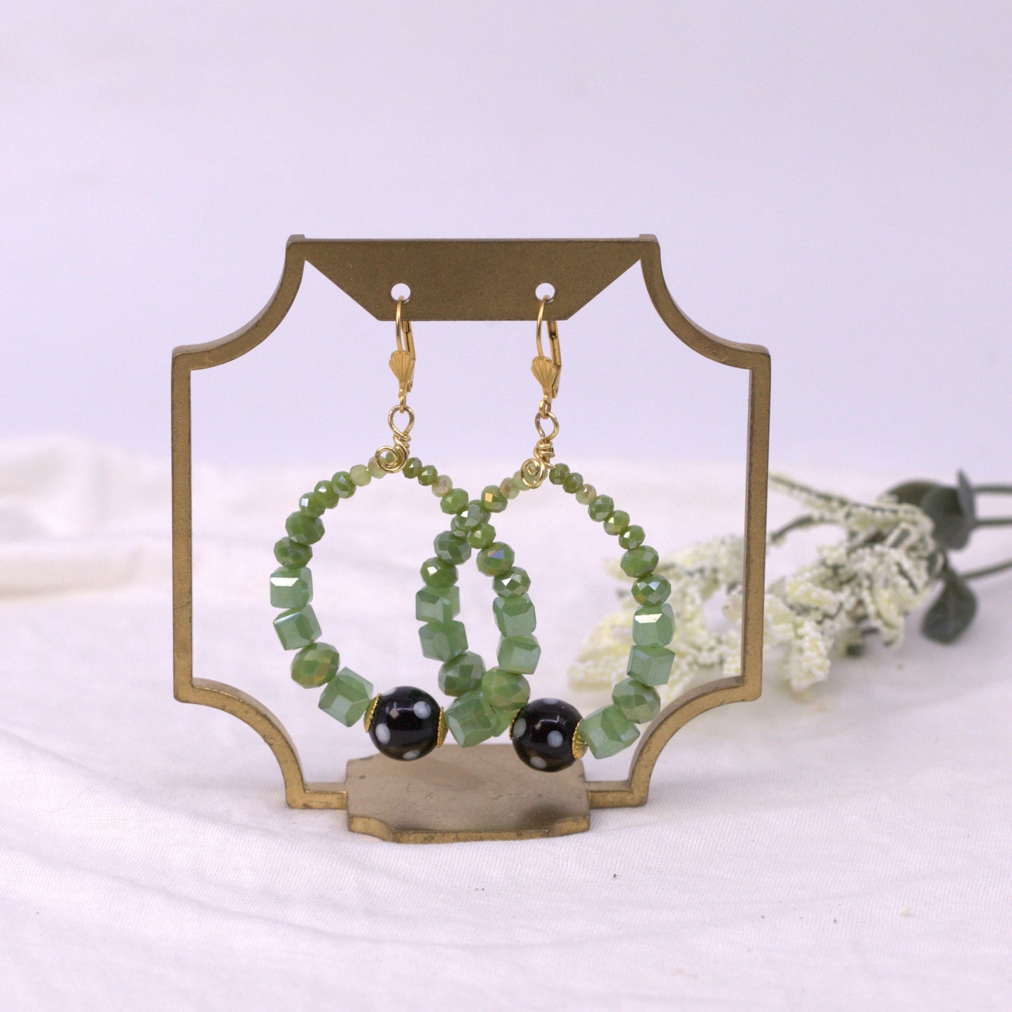 Green beaded earrings with black stones on a decorative stand against a white background