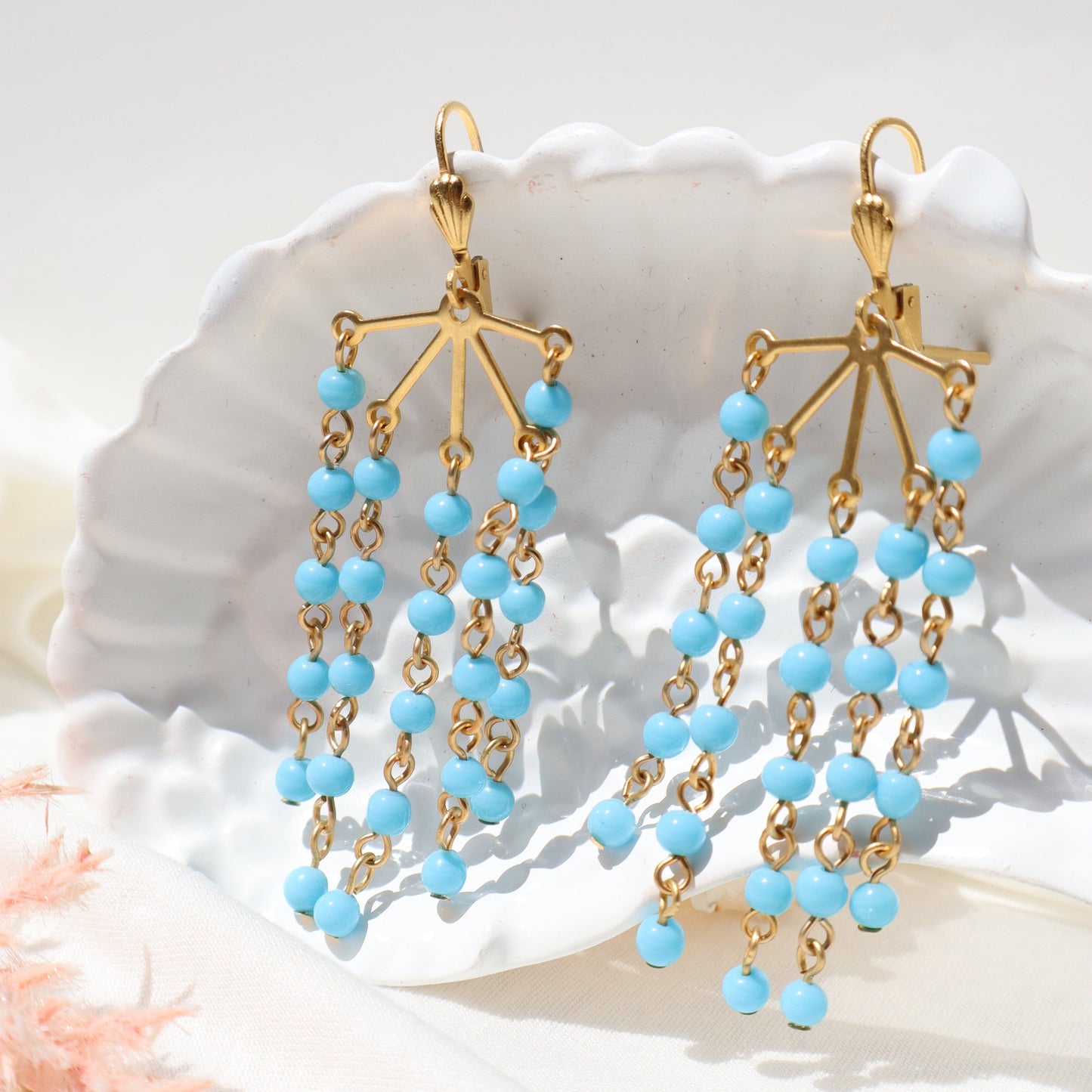 Gold and blue beaded earrings on a white shell background