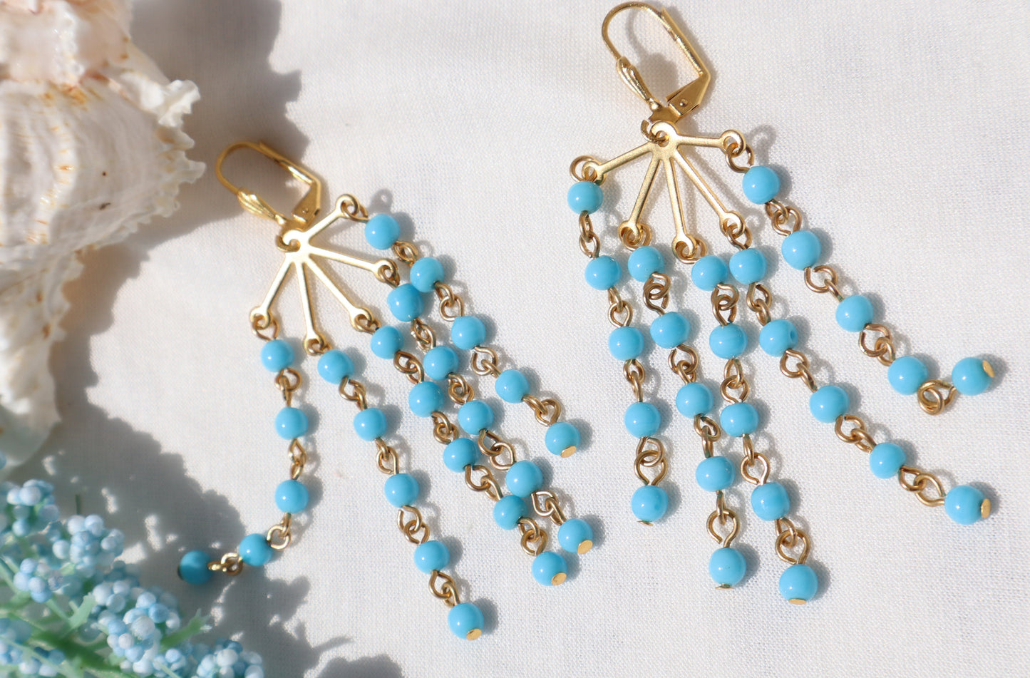 Gold and turquoise beaded earrings on a white background with floral elements.