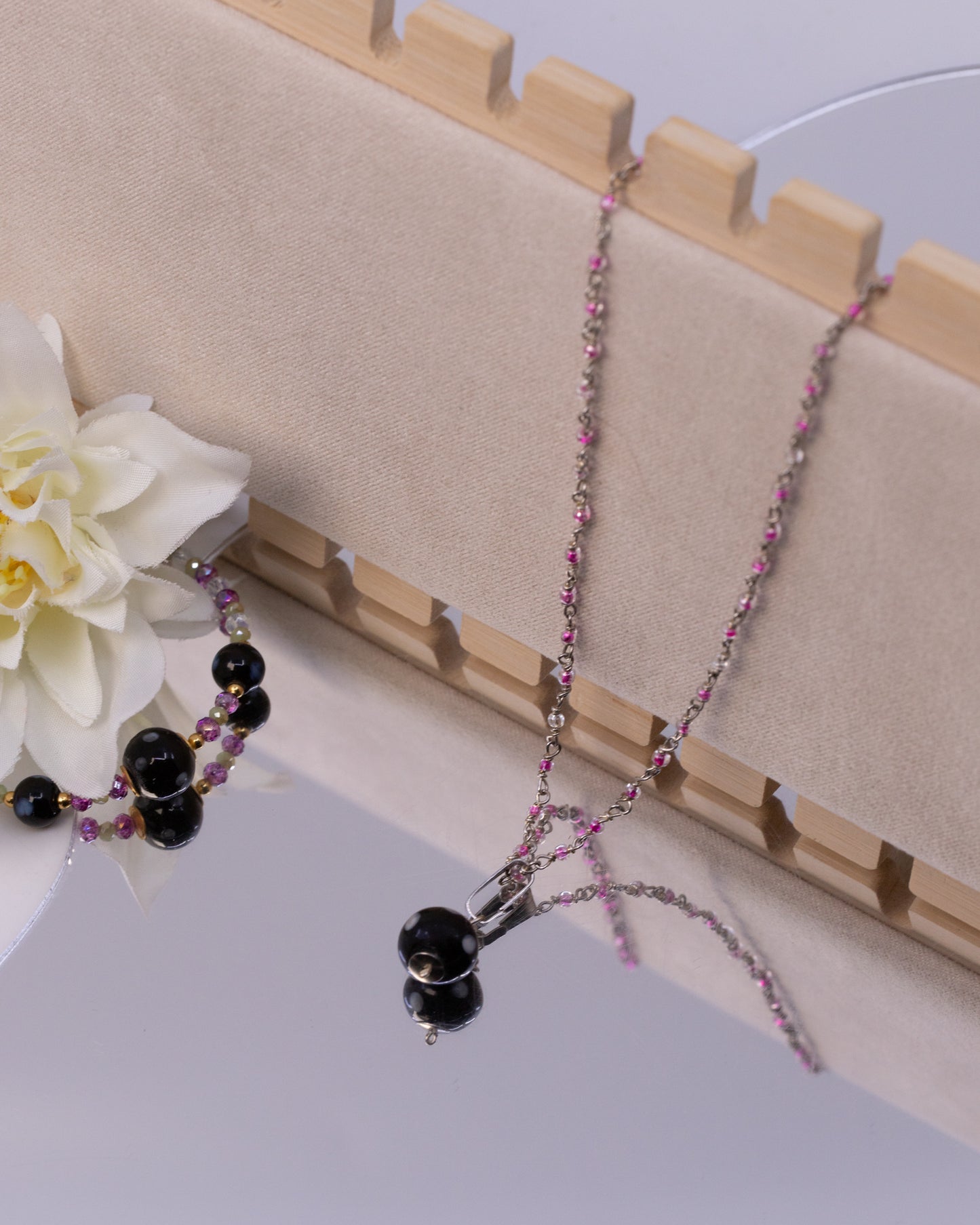 Necklace with black and pink beads on a wooden stand with a white flower.