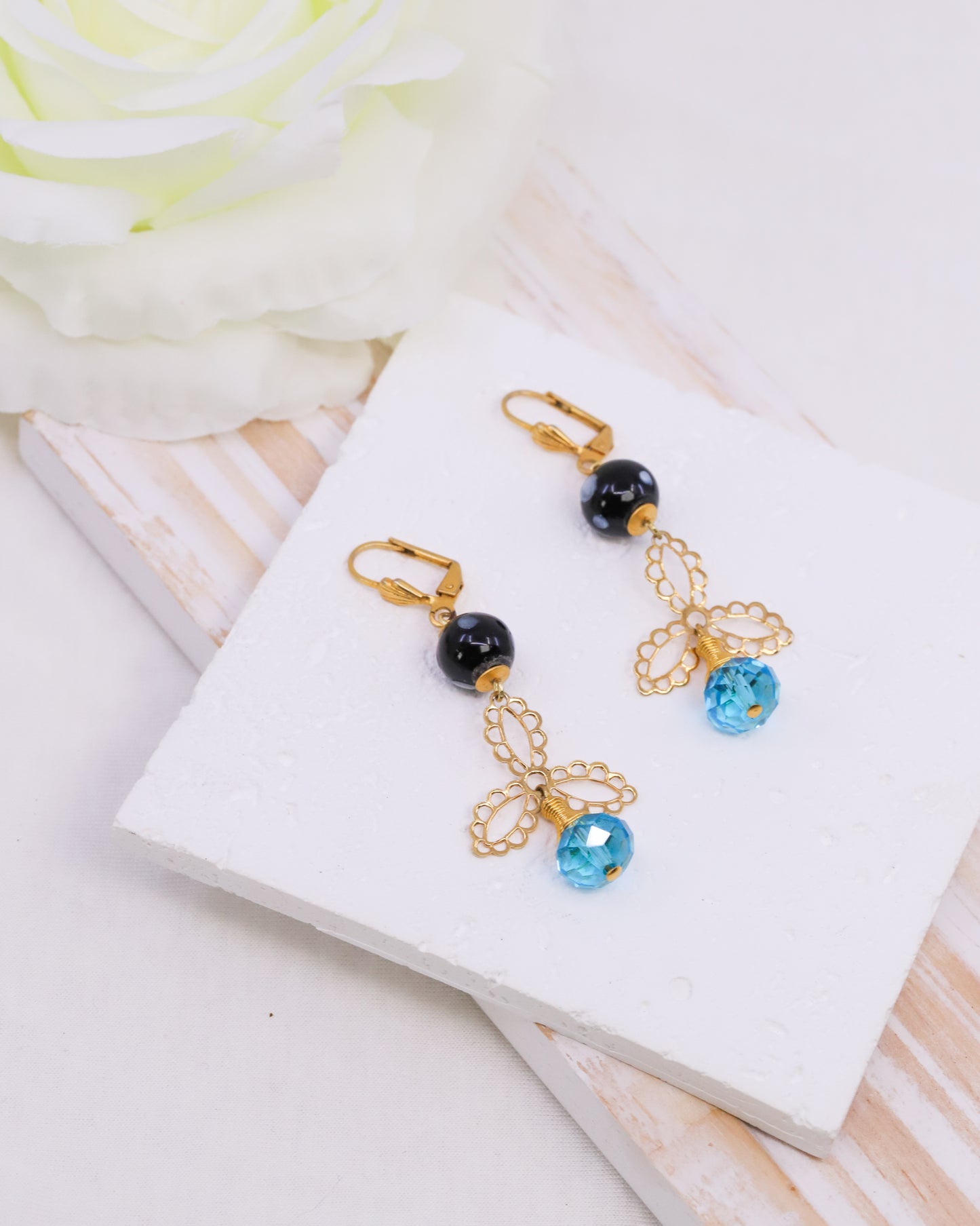 Pair of gold earrings with blue and black beads on a white box
