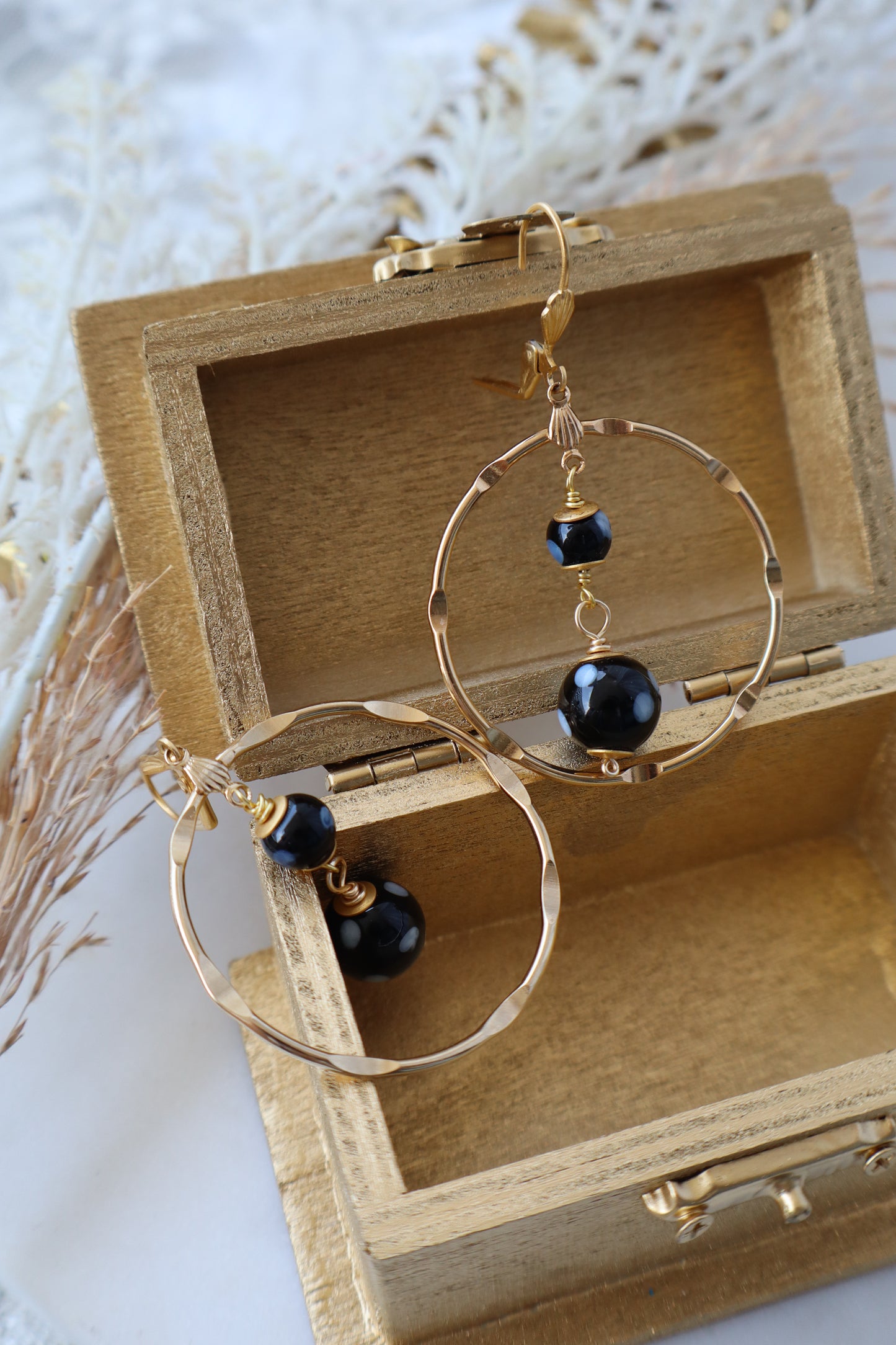 Gold hoop earrings with black beads in a wooden box on a light background