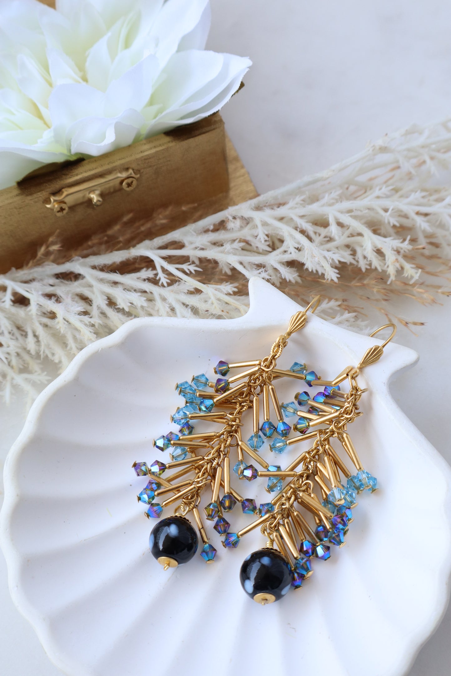 Gold necklace with blue and black beads on a white shell with flowers and wood piece.