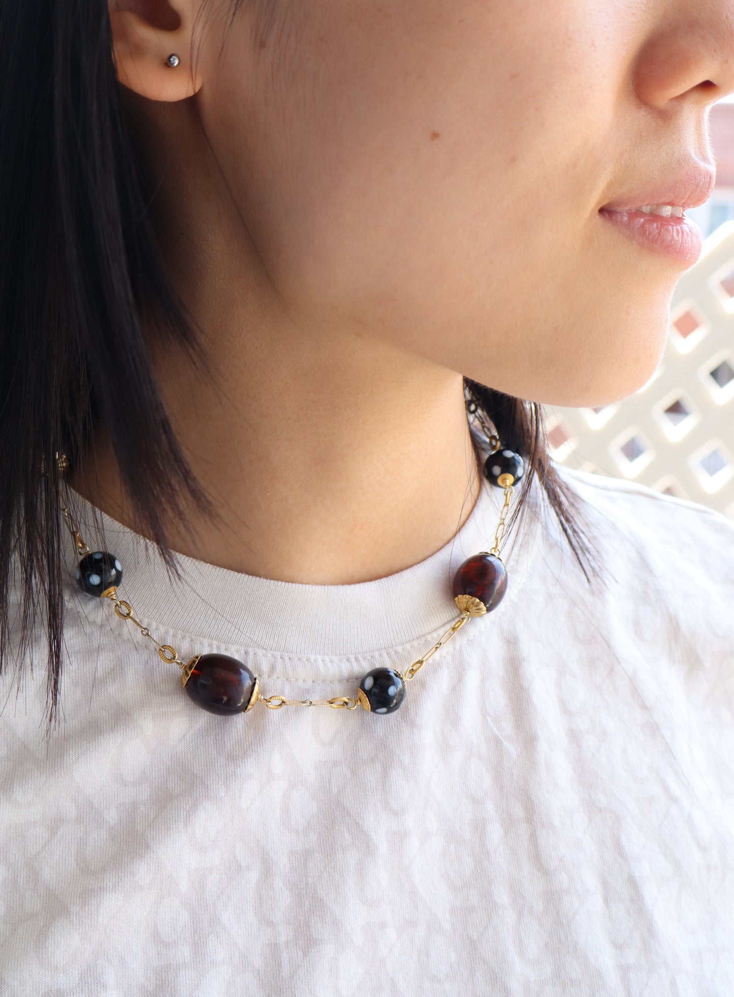 Close-up of a person wearing a necklace with dark beads and gold chain.