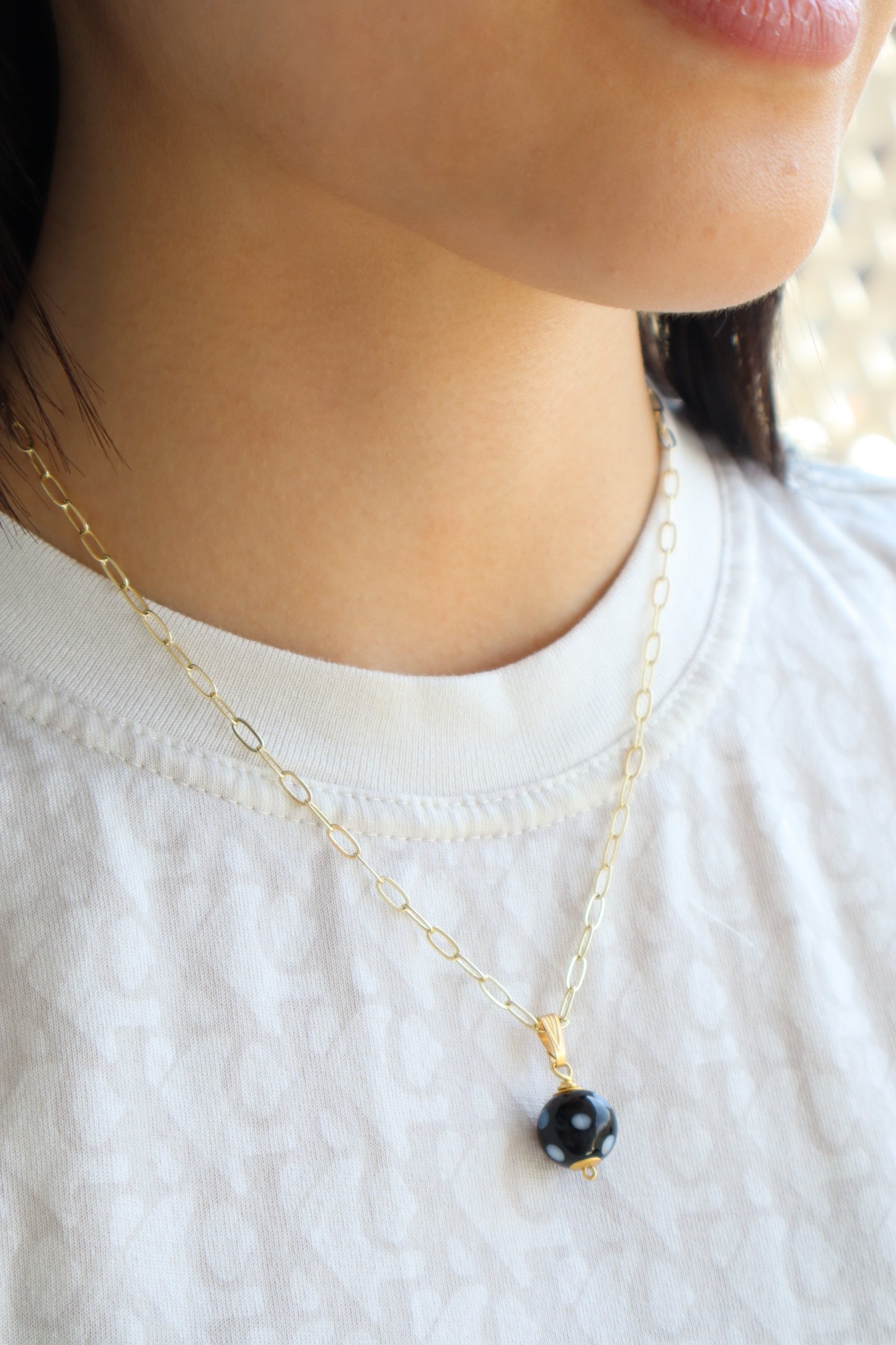 Close-up of a gold necklace with a black bead on a white background