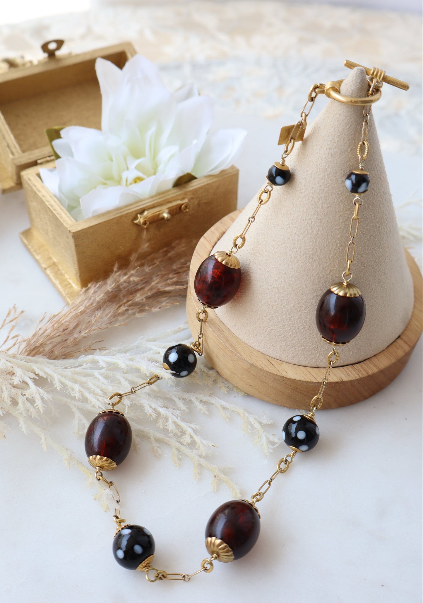 Necklace with brown beads and gold chain on a decorative stand with flowers and leaves.