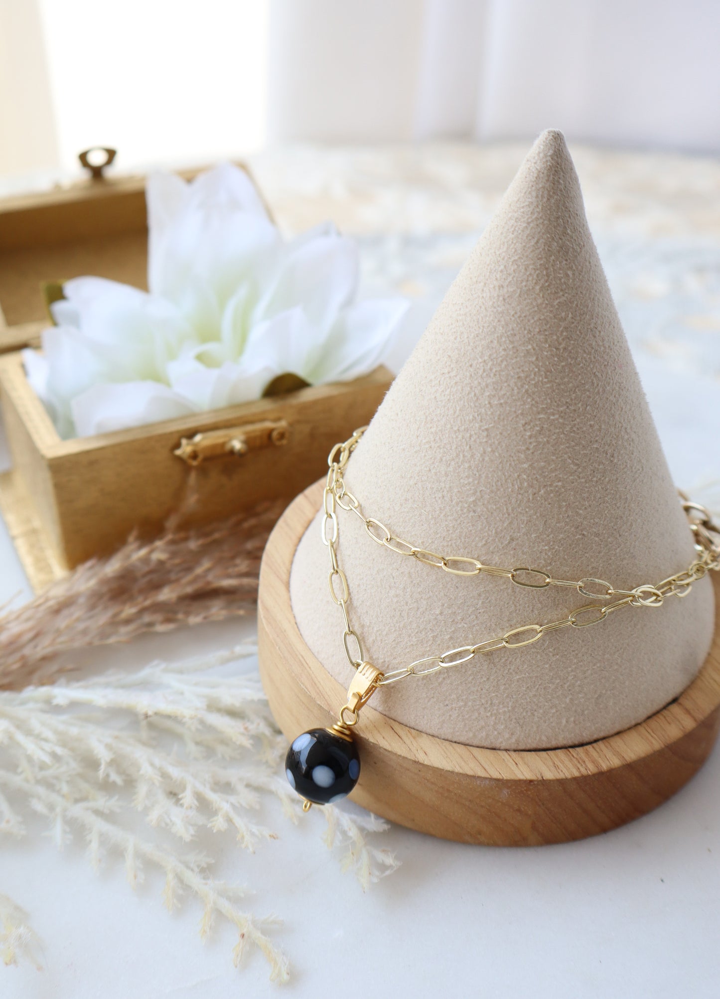 Necklace with a black bead on a beige cone-shaped jewelry stand with a wooden base.