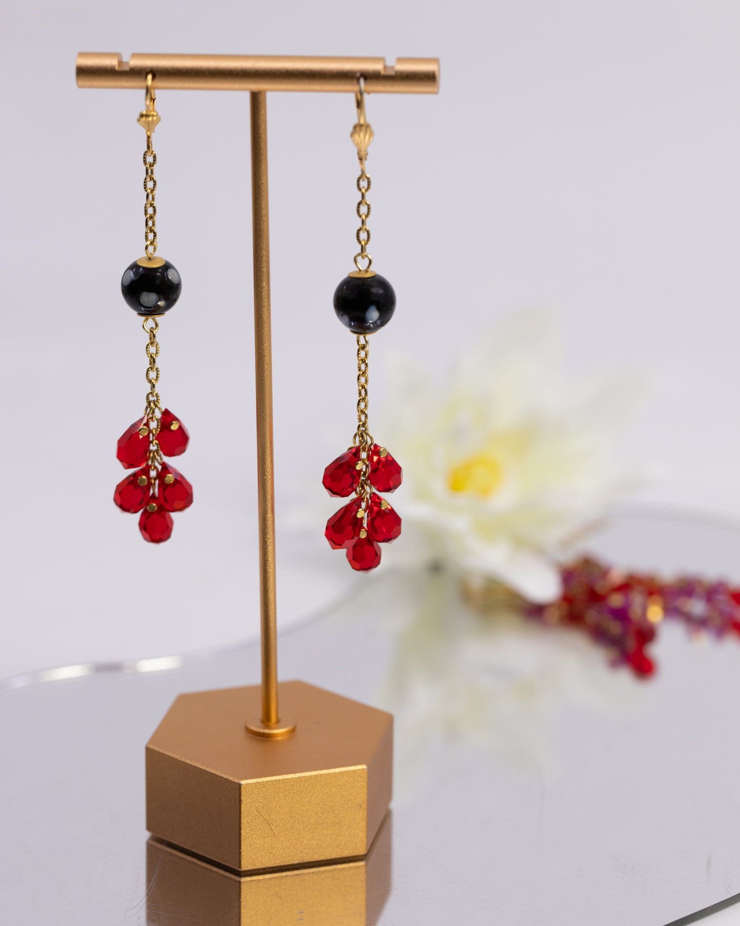 Pair of earrings with red beads and black stones on a gold stand.