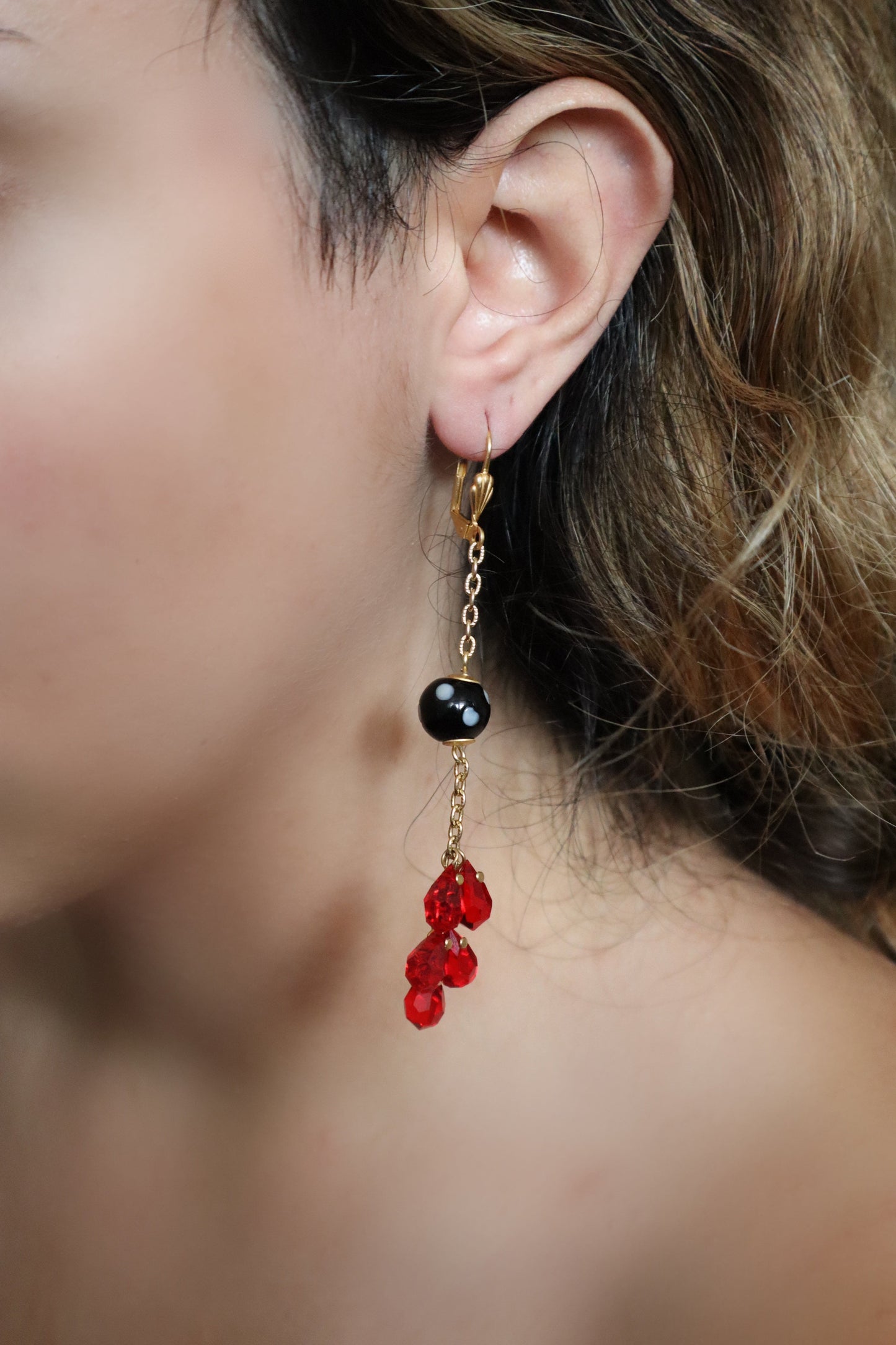 Close-up of an earring with red and black beads worn by a person.