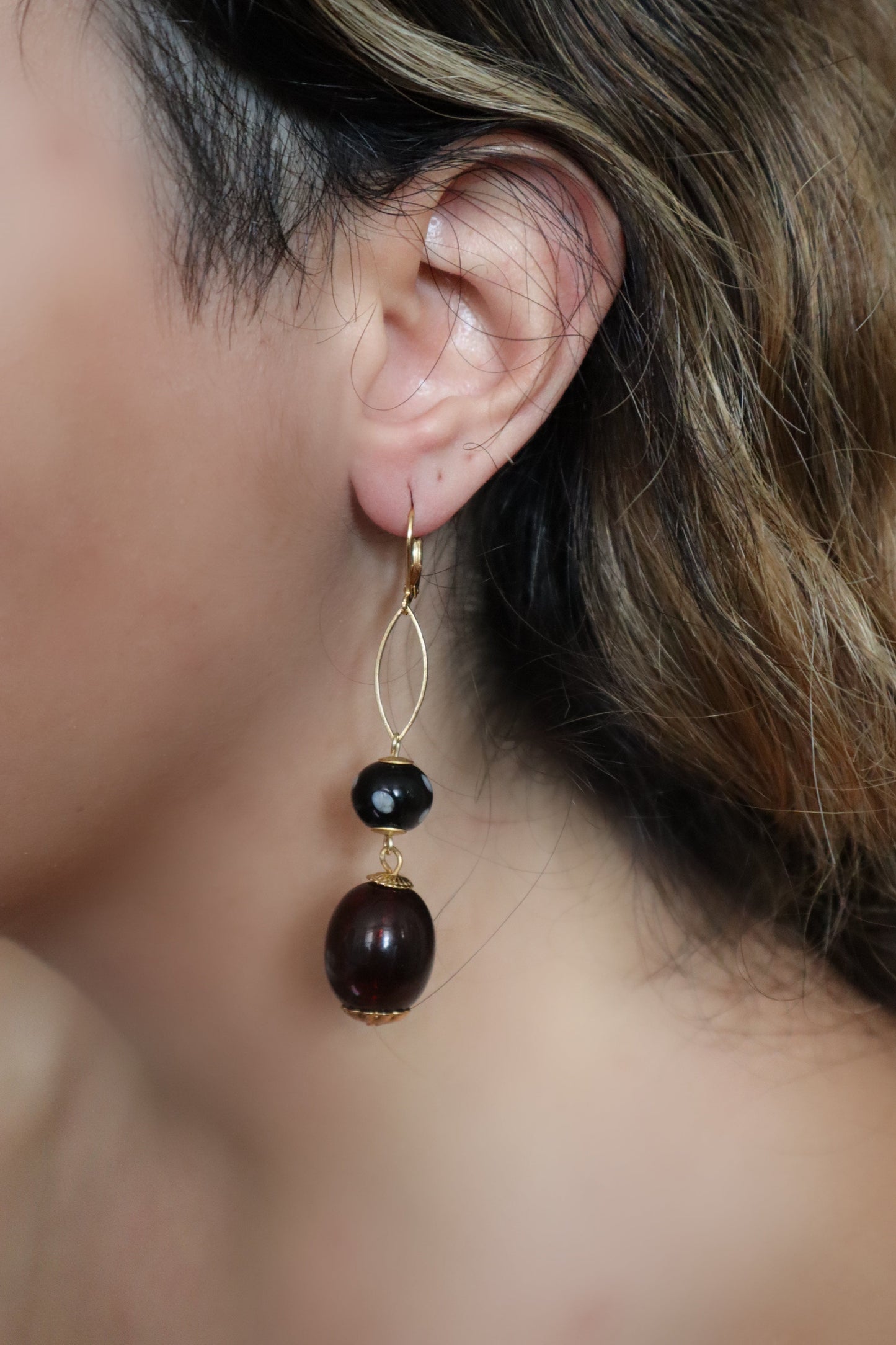 Close-up of an earring with a black bead and gold wire on a blurred background