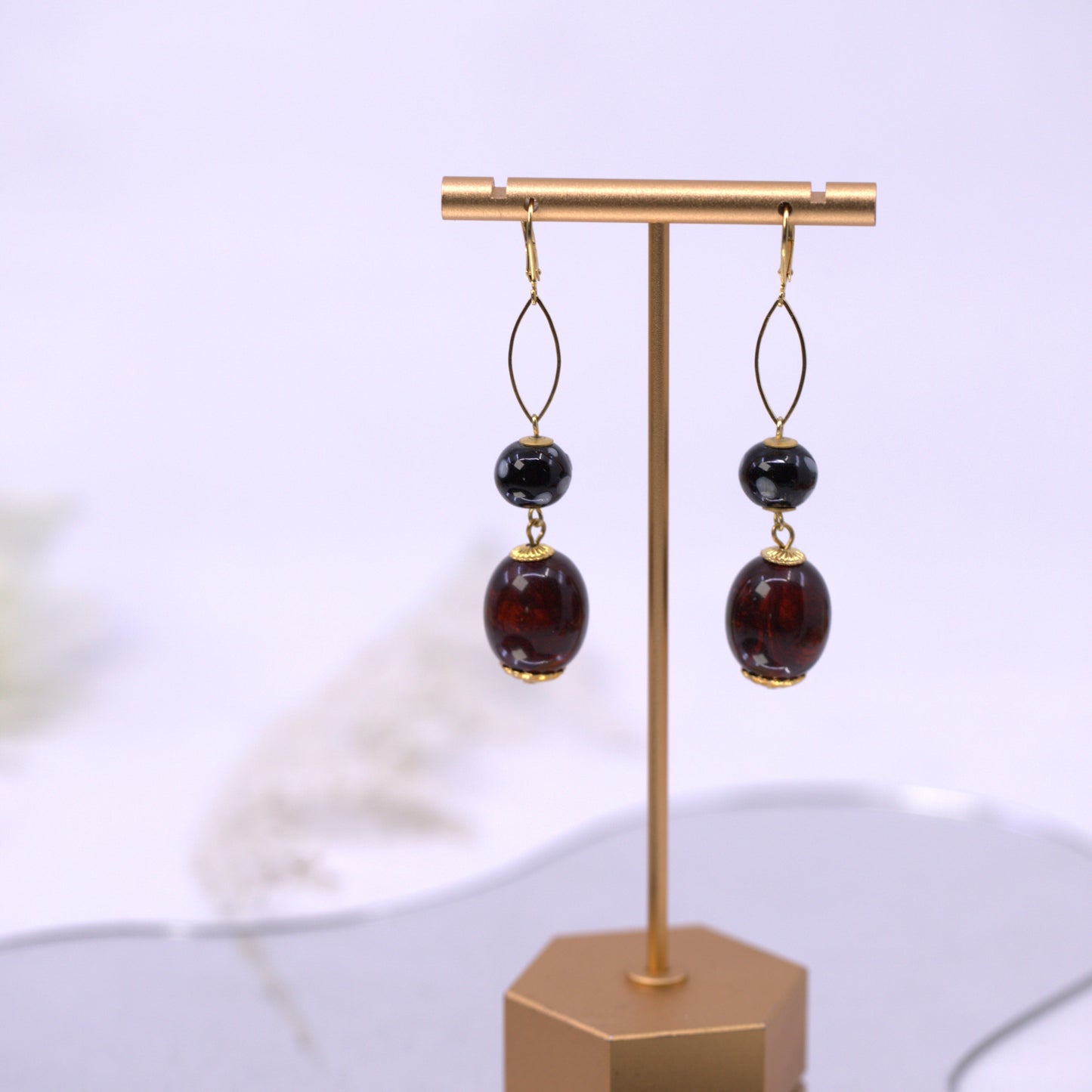Pair of earrings with dark beads on a gold stand against a light background