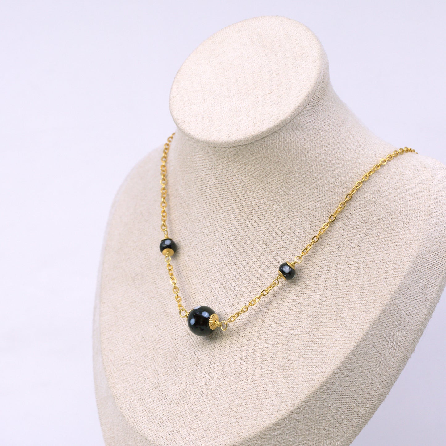 Gold necklace with black beads on a mannequin bust against a light gray background