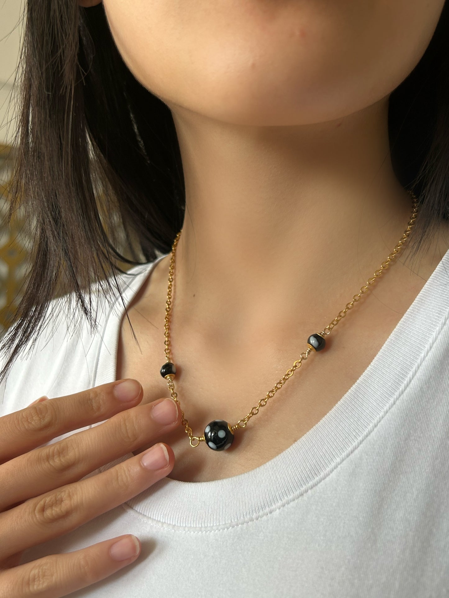 Gold necklace with black beads worn by a person on a plain background
