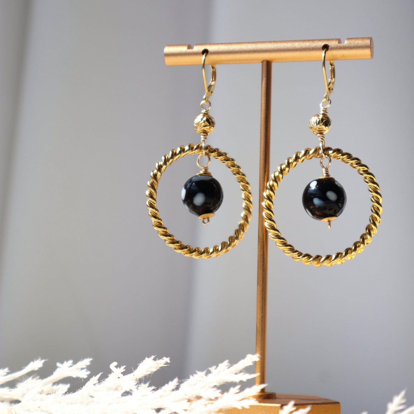 Gold hoop earrings with black beads on a gold stand against a gray background