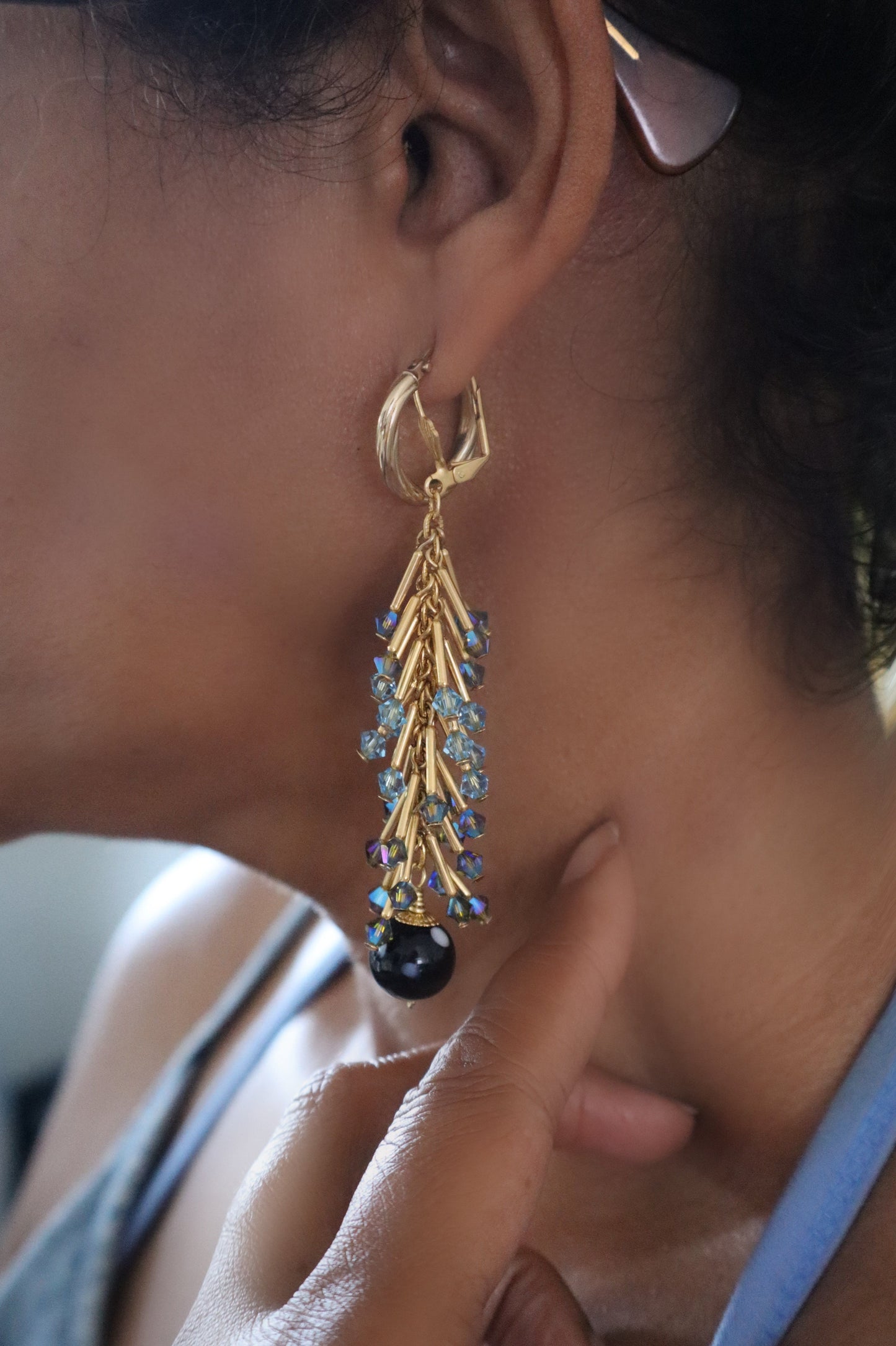 Close-up of a person wearing a gold earring with blue stones and a black bead.