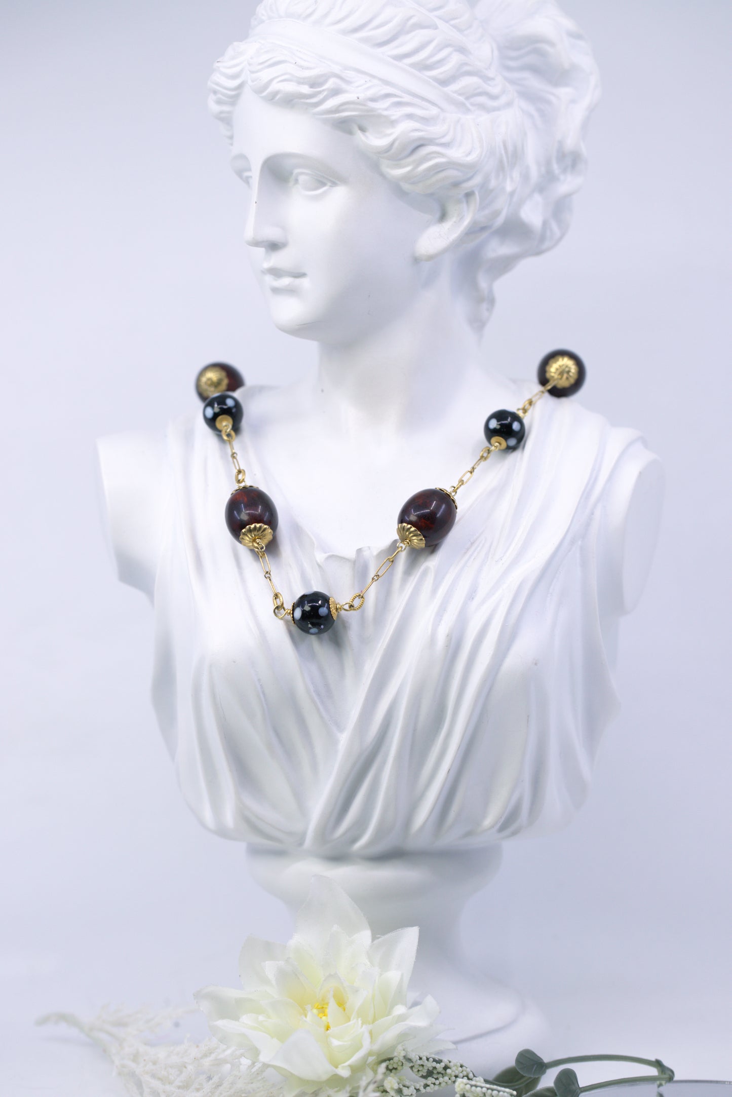 Necklace with black and gold beads on a classical bust against a white background