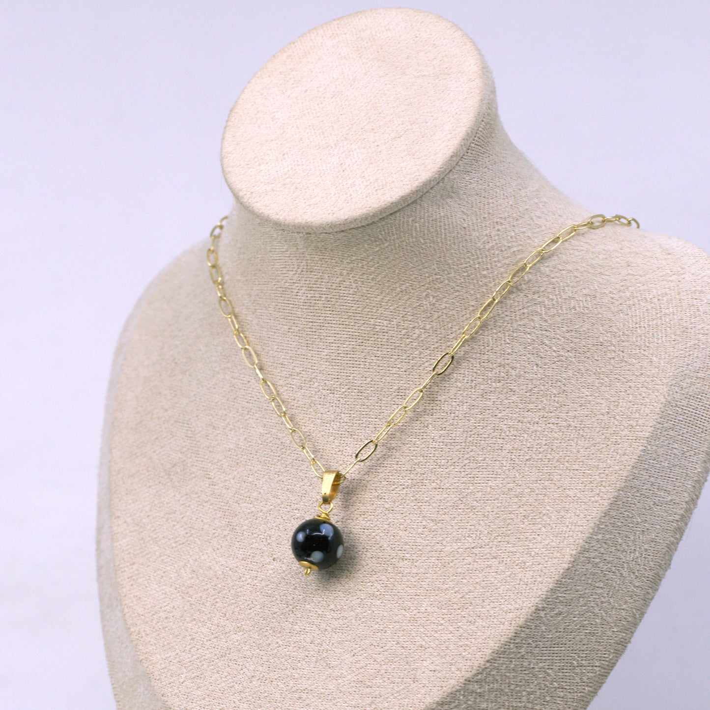 Gold necklace with a black pendant on a mannequin bust against a light purple background