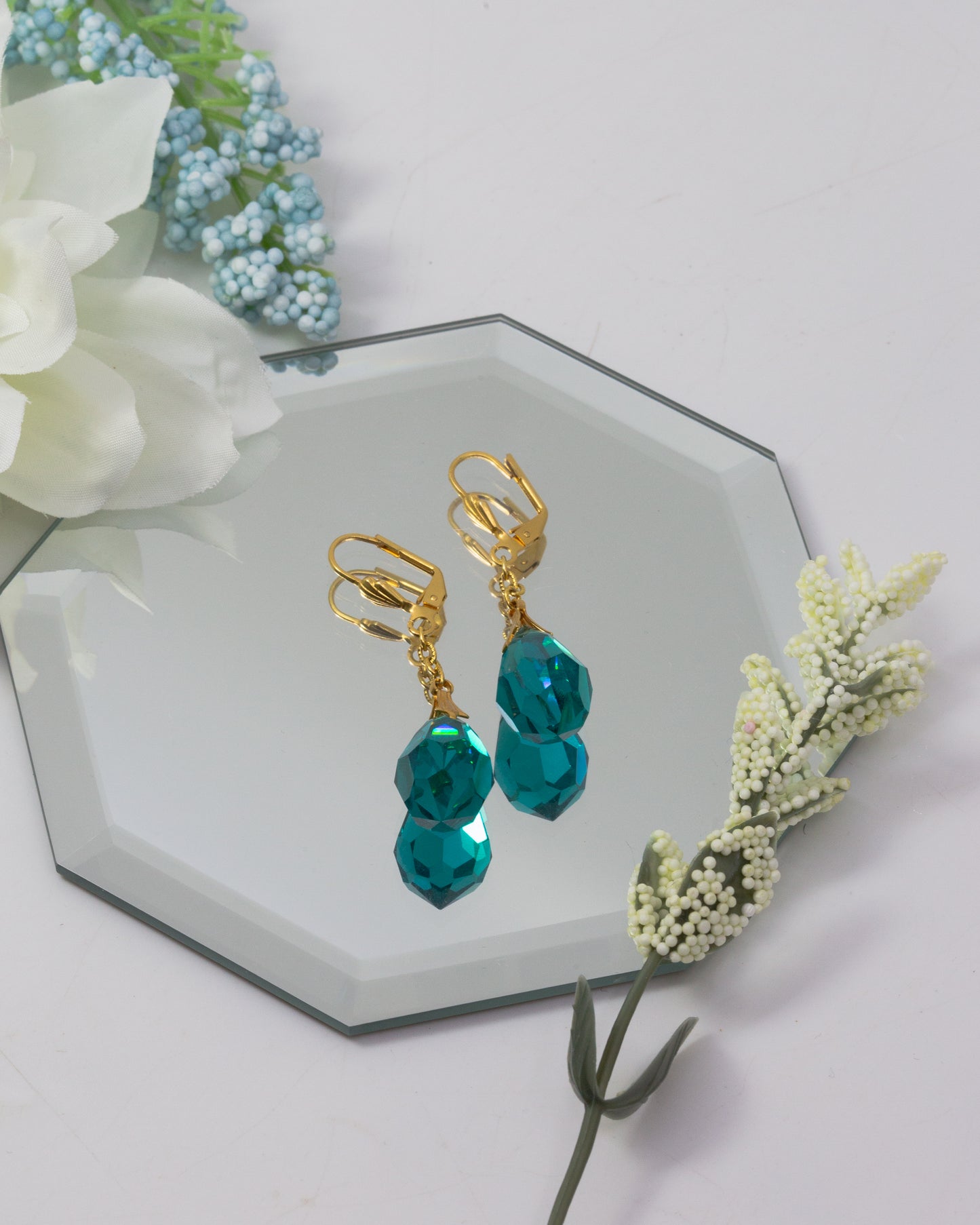 Gold earrings with teal beads on a decorative stand with flowers.