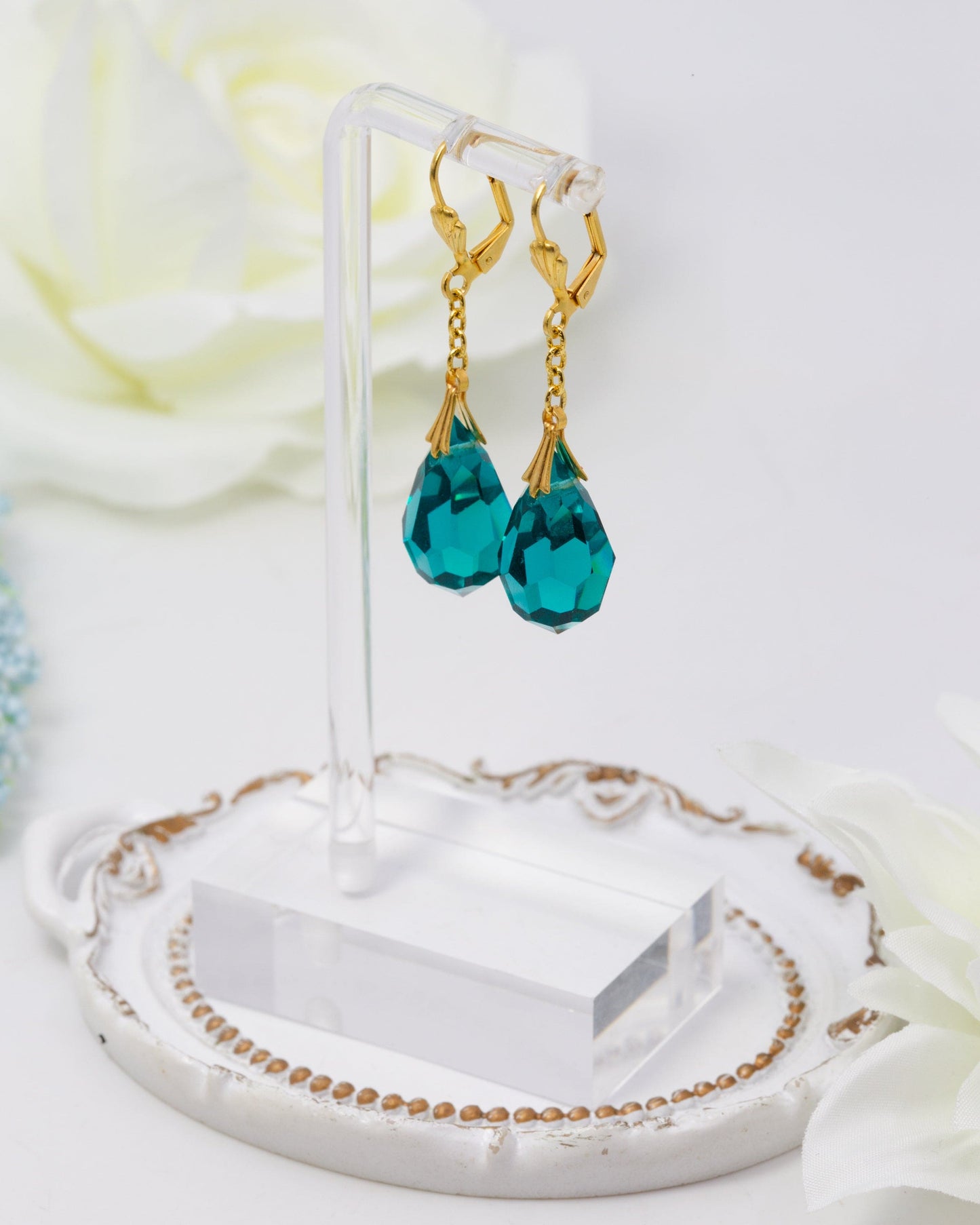 Teal teardrop earrings with gold hooks on a clear stand against a white background
