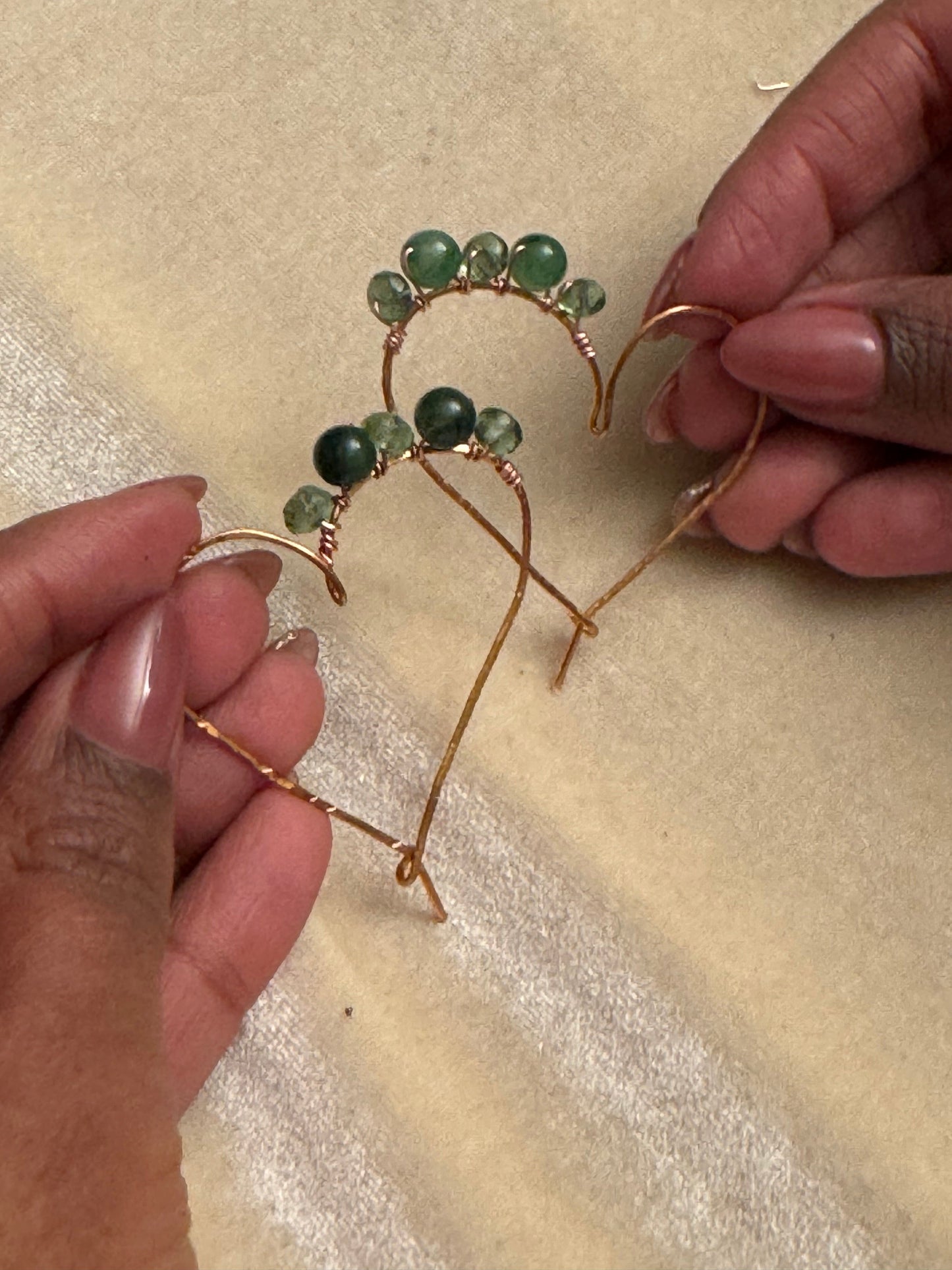 Hands assembling green beaded hoop earrings using gold wire during a jewelry class