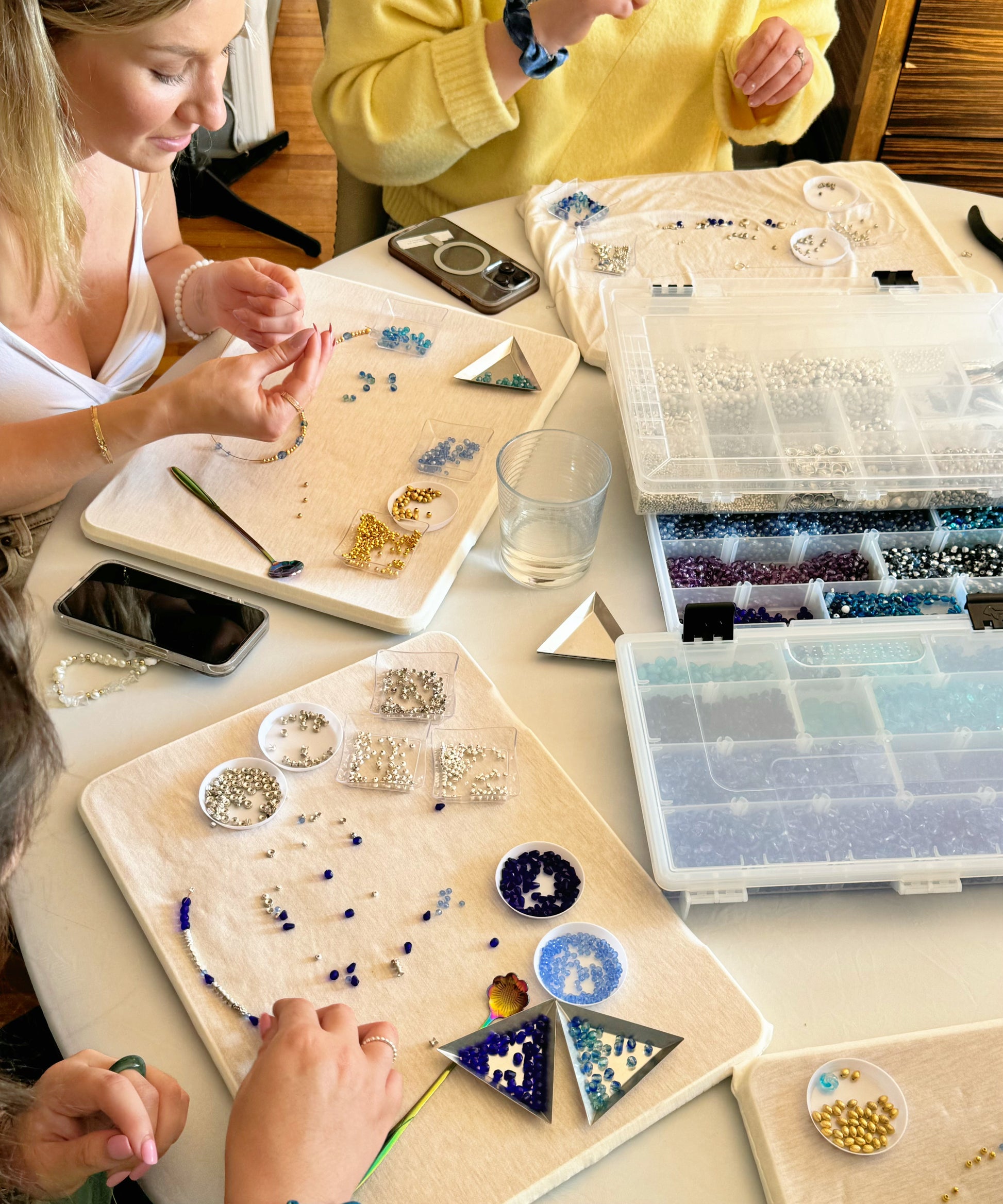 Hands of multiple participants choosing beads and designing necklaces during a creative jewelry-making class
