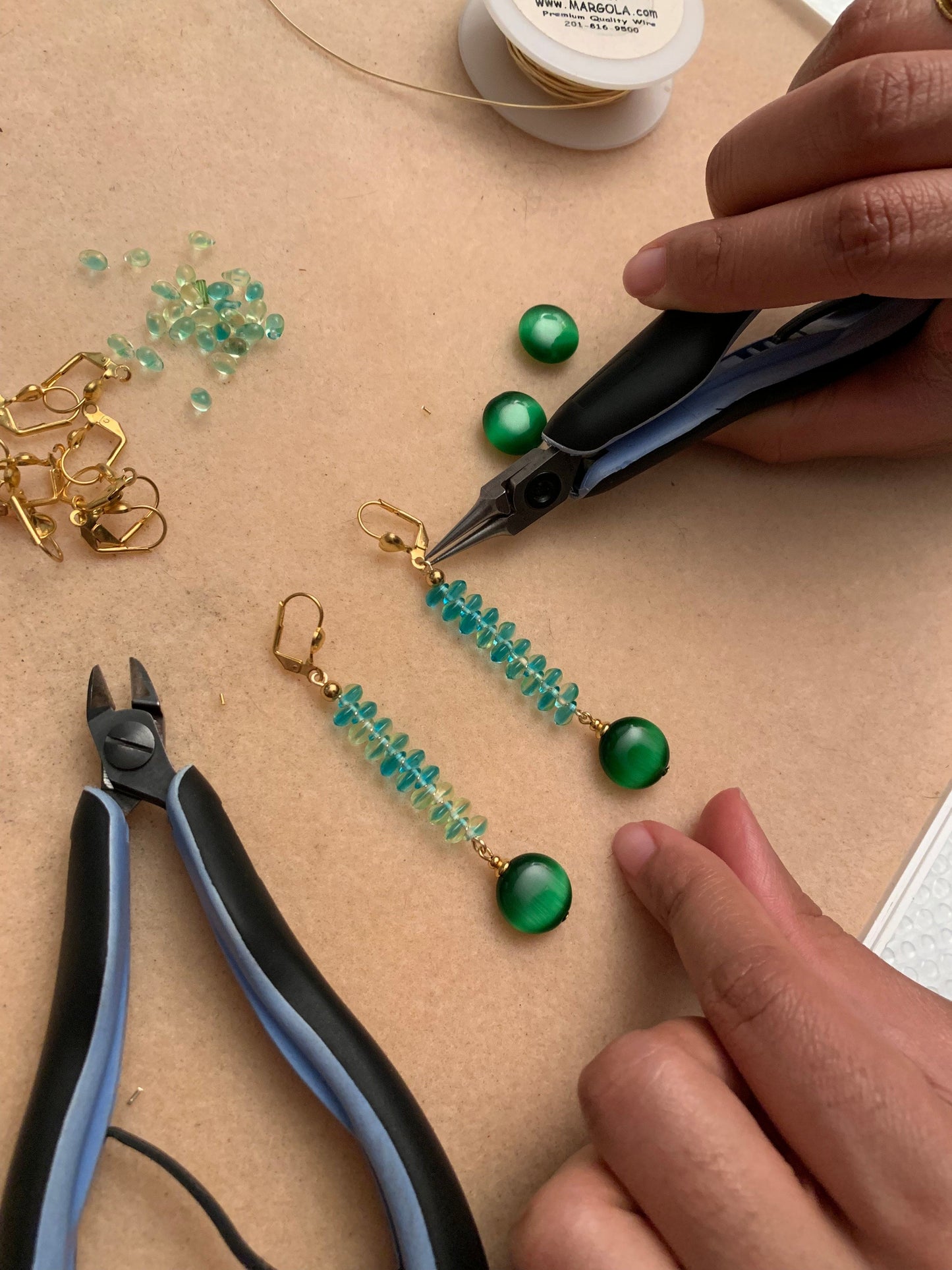 Flat lay of green beads, wire, and pliers used in a hands-on earring making class