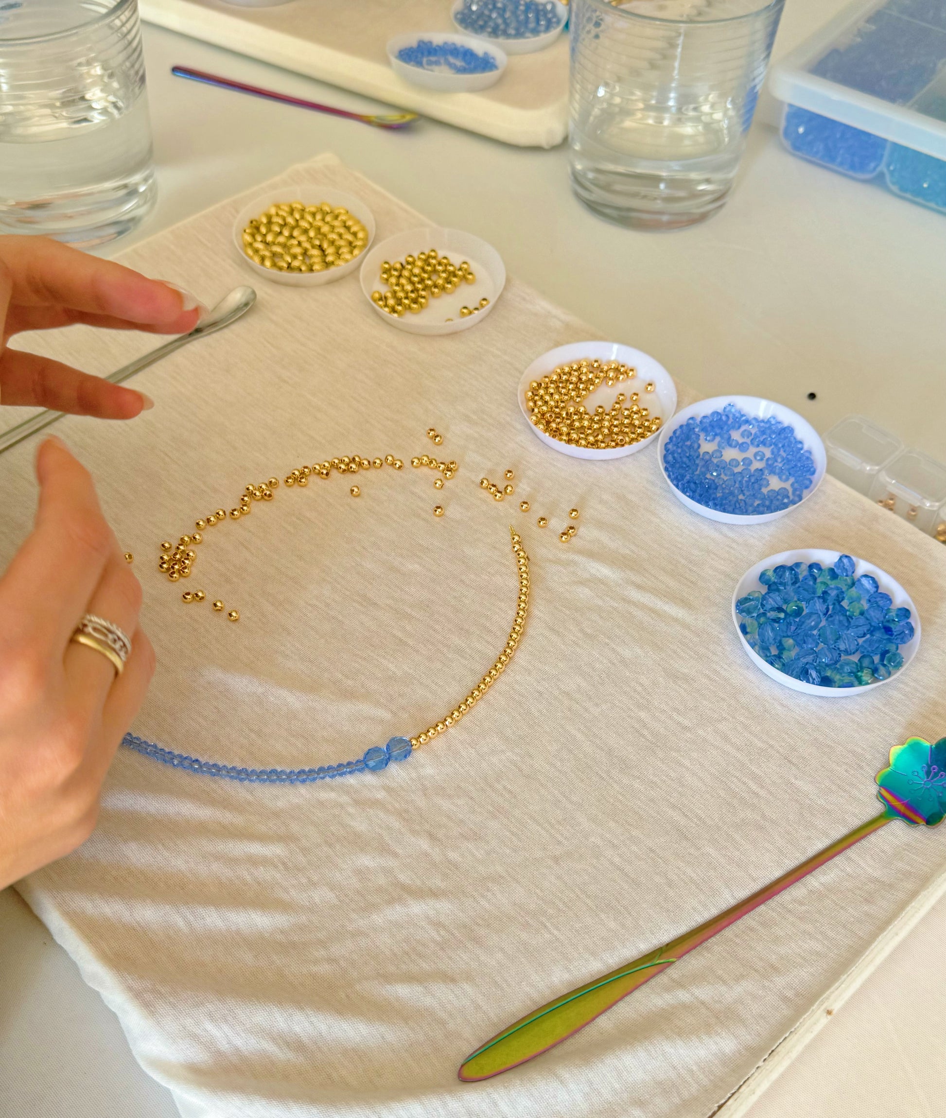 Hands laying out necklace pattern with blue and gold beads during DIY jewelry class
