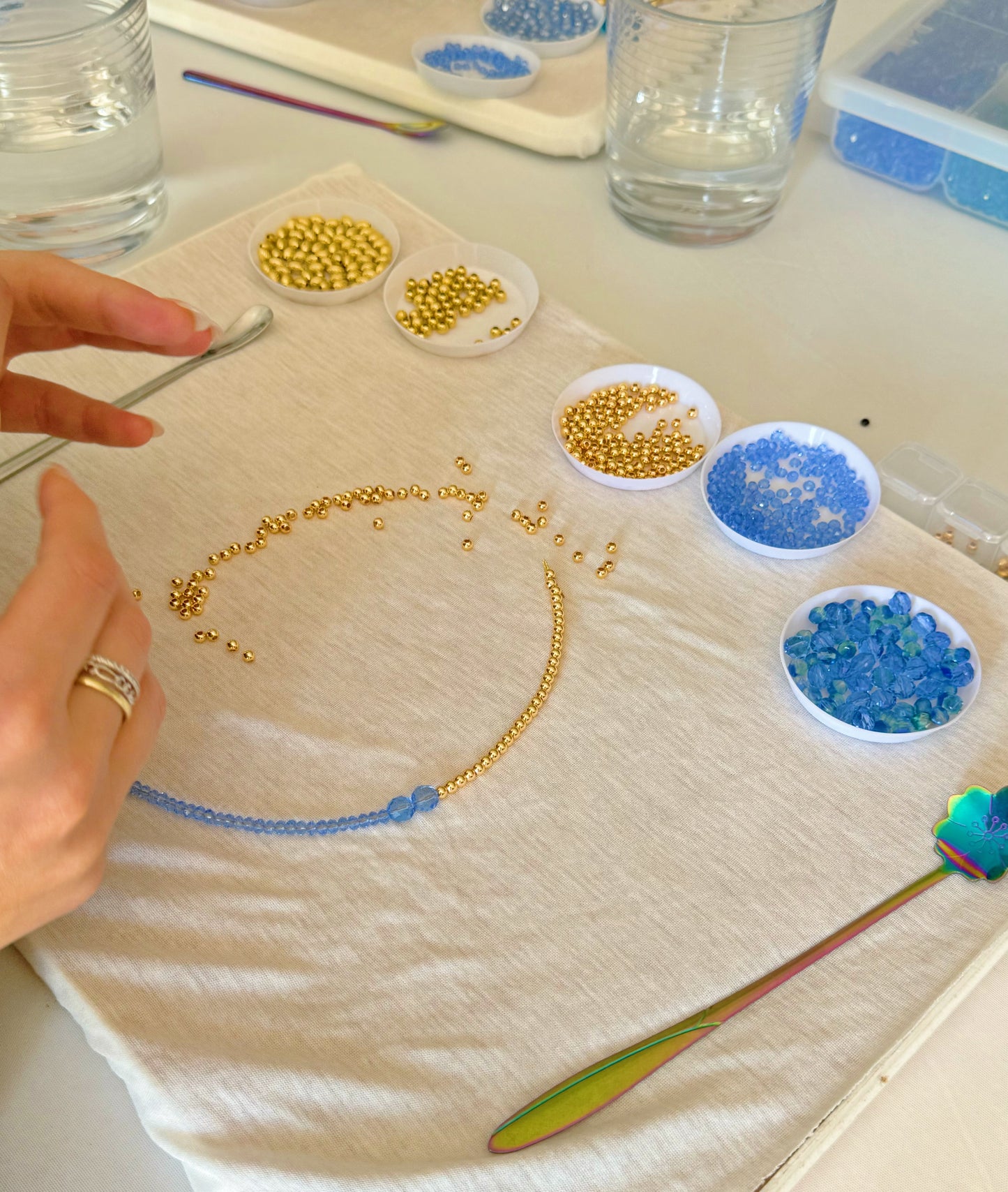 Hands laying out necklace pattern with blue and gold beads during DIY jewelry class