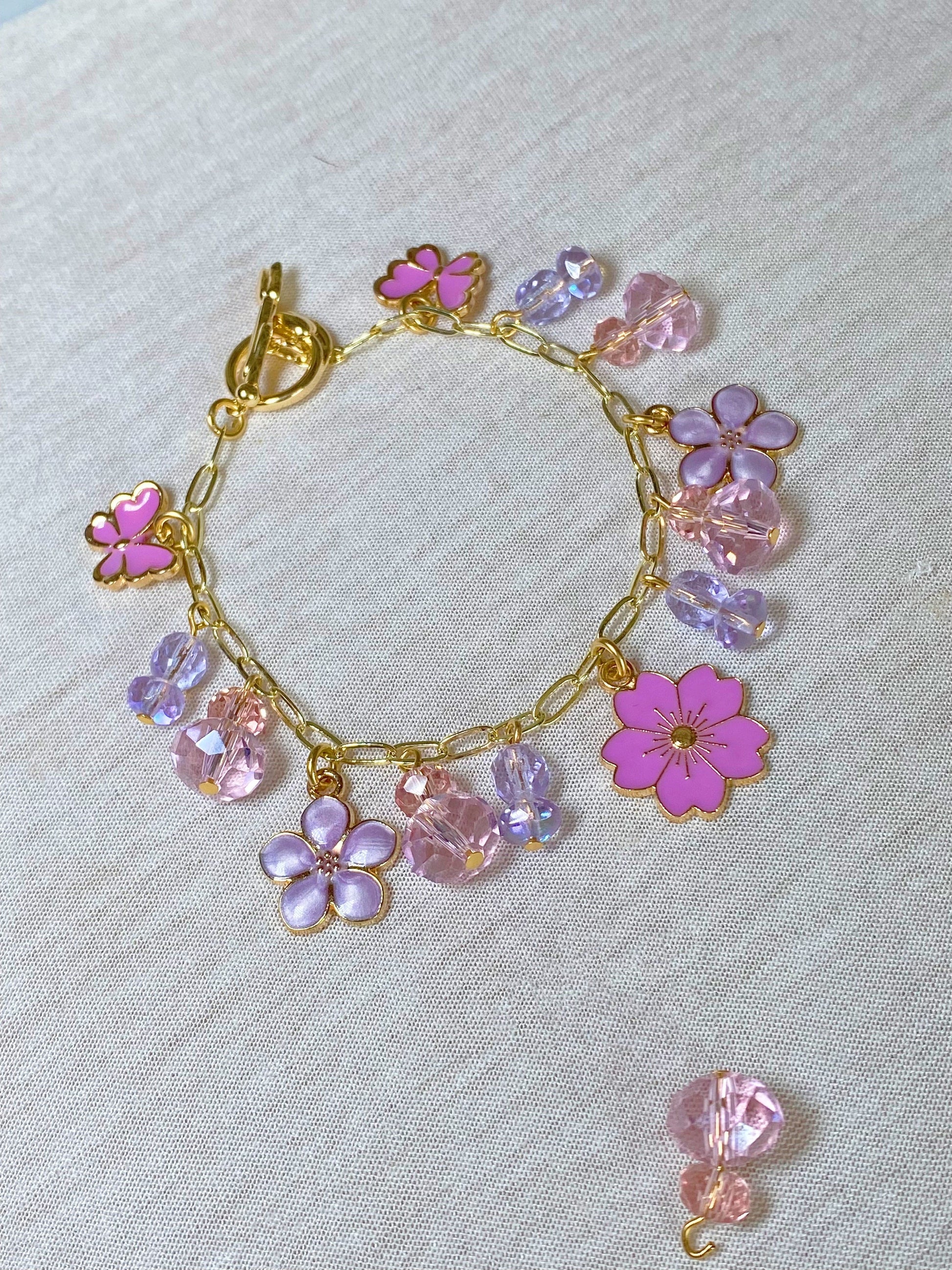 A handmade charm bracelet with pink enamel flowers and crystal beads, created in a DIY jewelry-making workshop