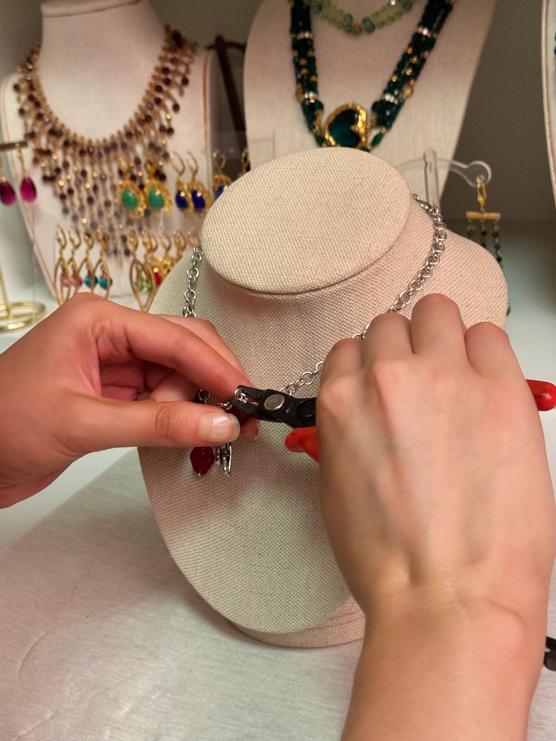 Hands using jewelry pliers to attach final charms to a handmade chain necklace during a DIY jewelry-making class in NYC
