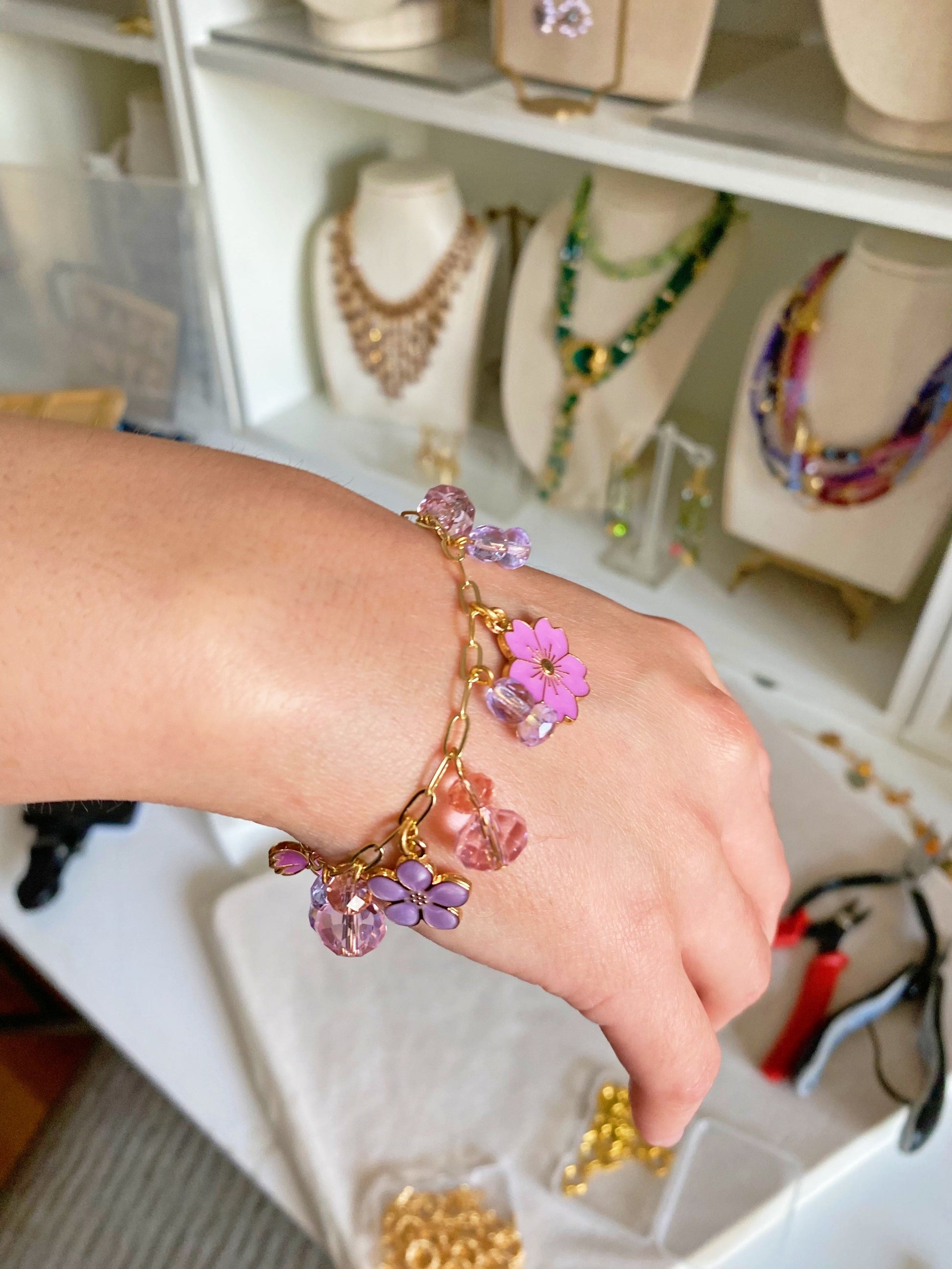 A student showcasing a handmade floral charm bracelet featuring pink and purple beads, created during a DIY jewelry making class in NYC