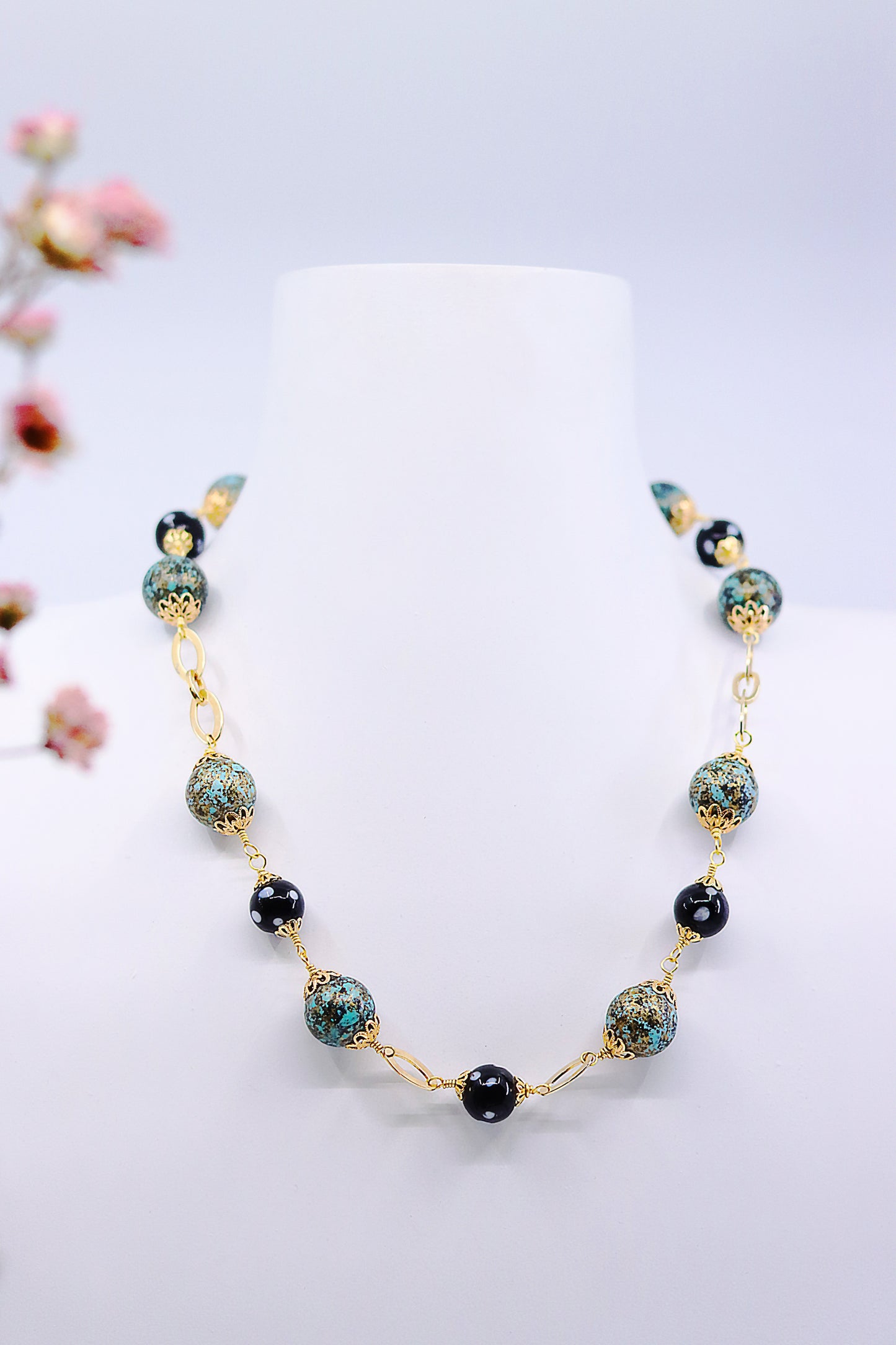 Handcrafted Alcidia Necklace displayed on jewelry stand with turquoise and black beads, gold-plated chain
