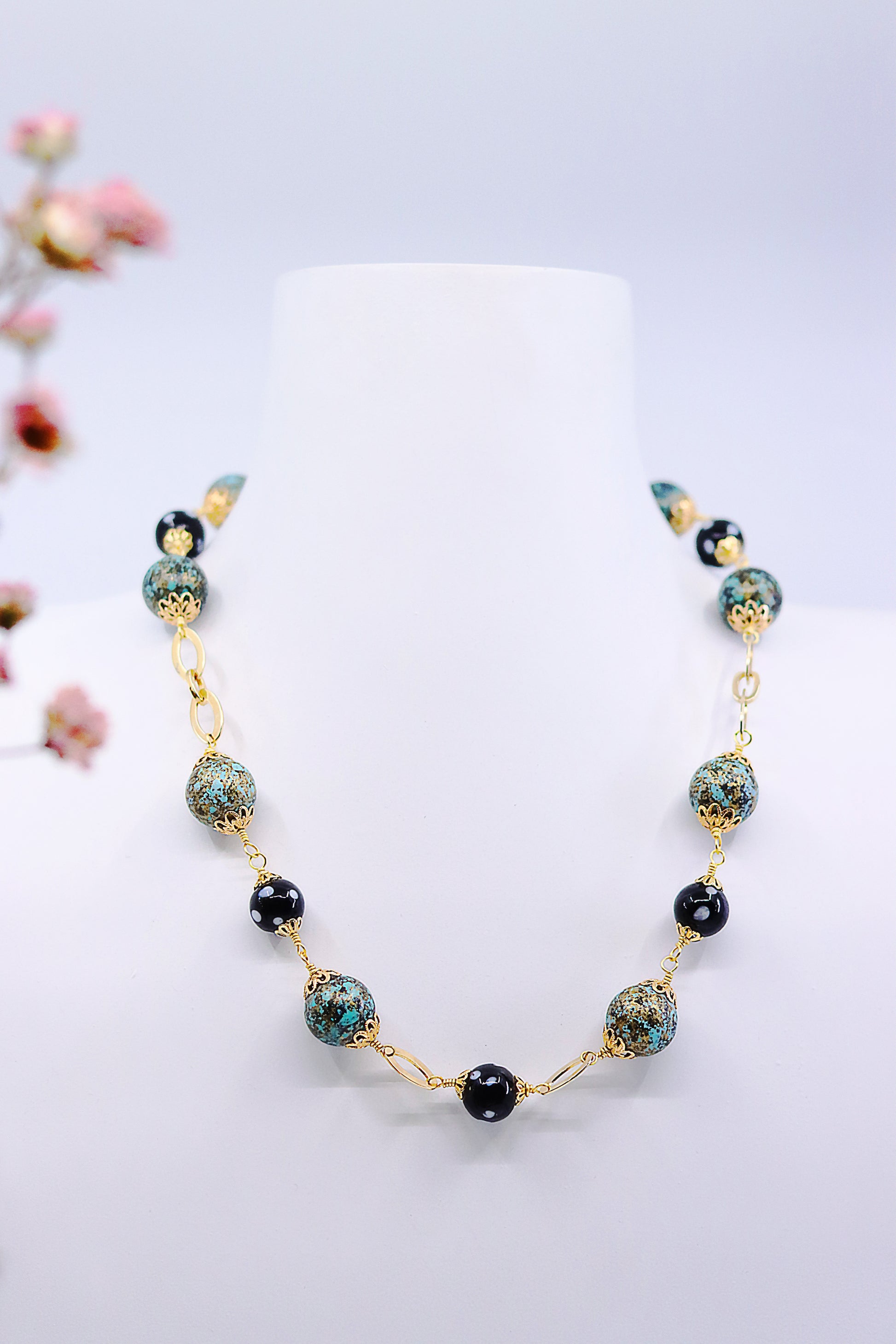Handcrafted Alcidia Necklace displayed on jewelry stand with turquoise and black beads, gold-plated chain