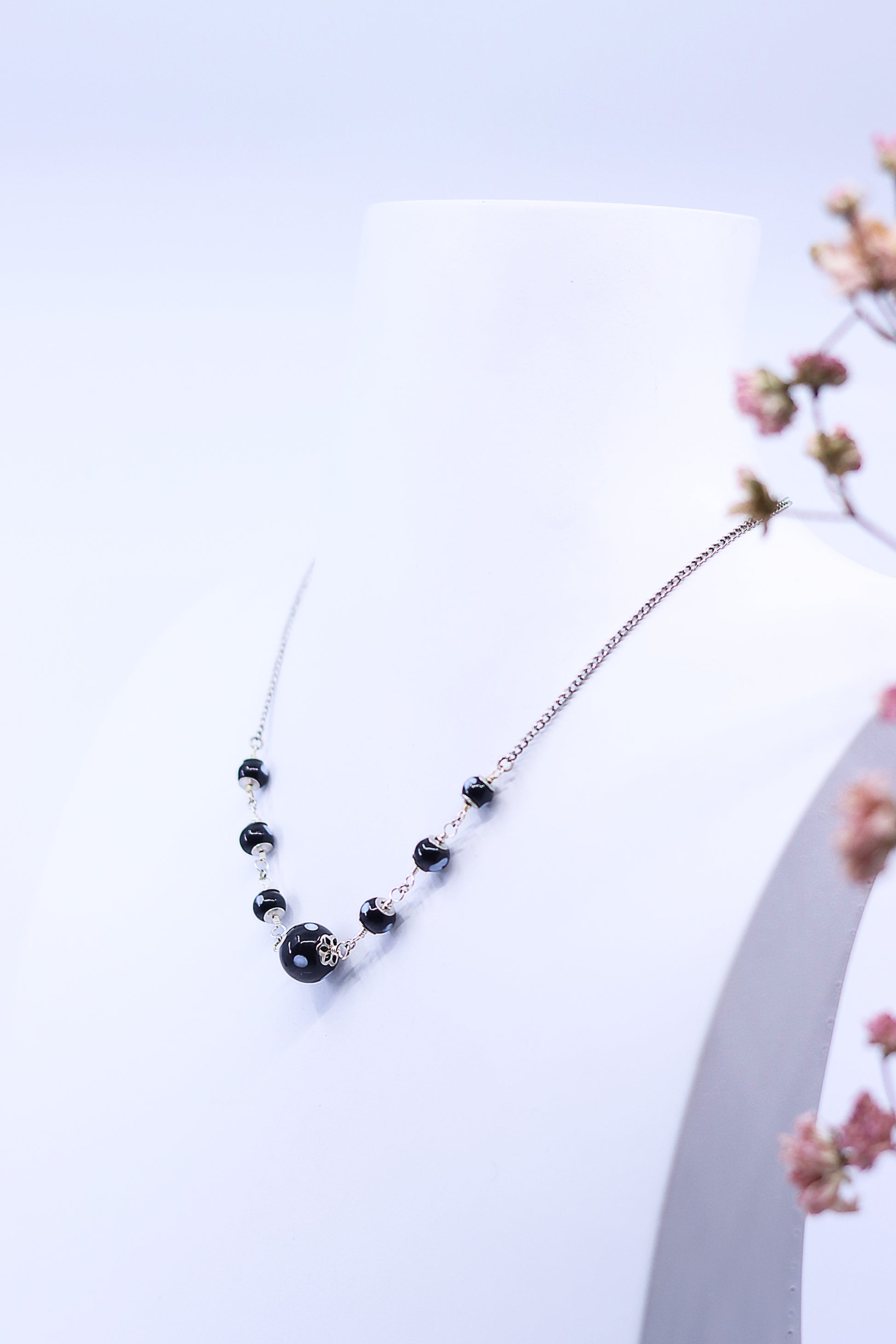 Maninha necklace worn on mannequin, featuring gold chain and black evil eye beads
