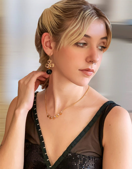 Model with sleek ponytail wearing Alzerina Jewelry gold drop earrings and black sequin dress, styled for long earrings.
