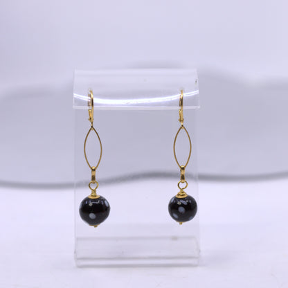 Black beaded earrings with gold hooks on a clear stand against a white background. evil eye earrings