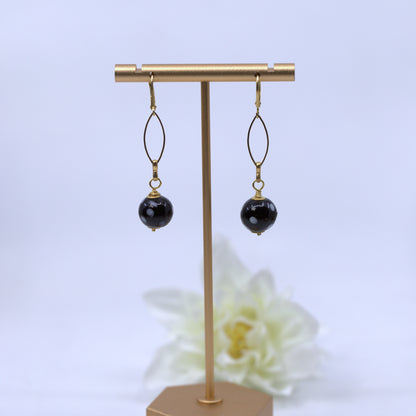 Black beaded earrings on a gold earring stand with a white flower in the background. Evil eye earrings