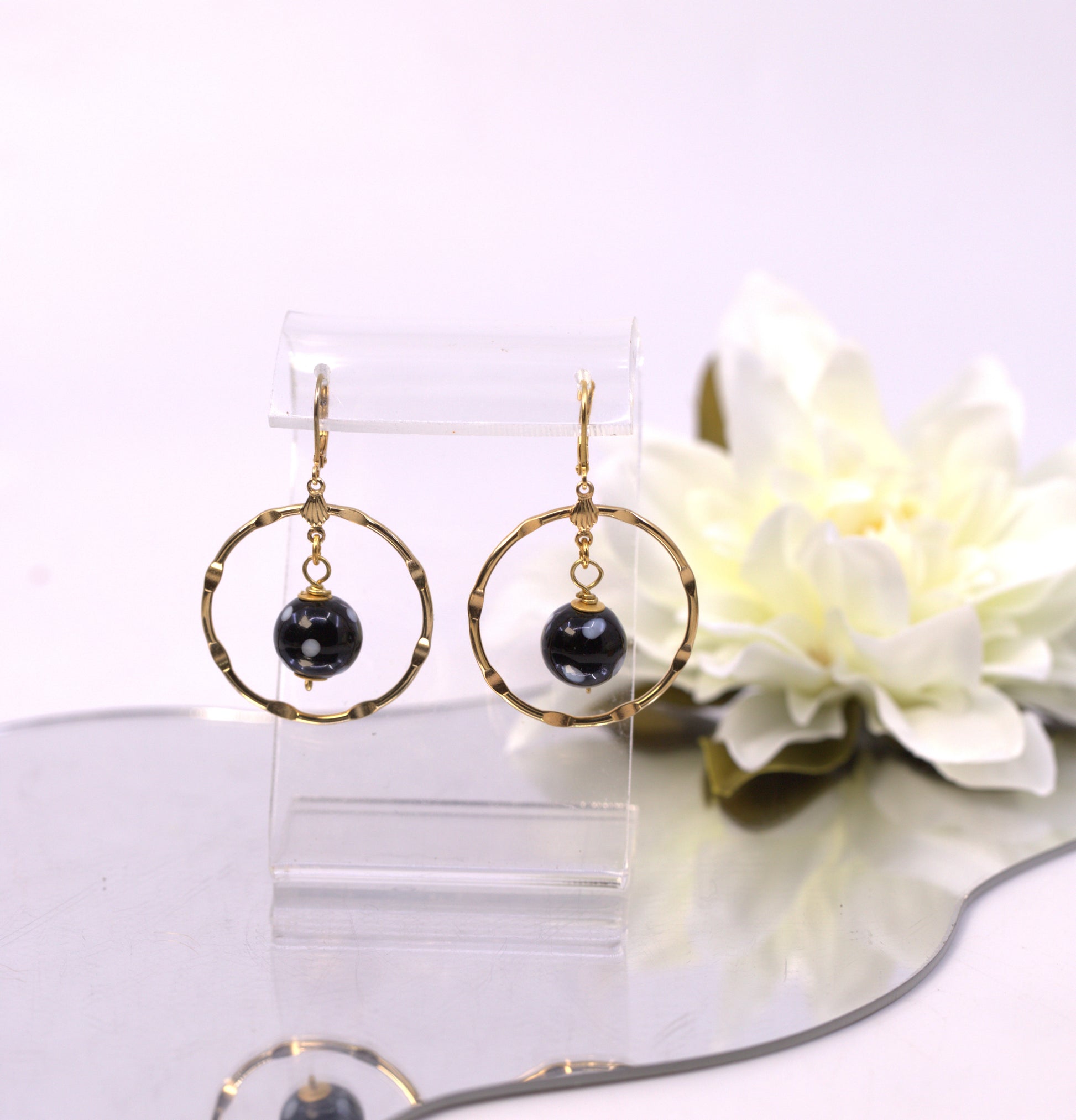 Gold hoop earrings with black beads on a clear stand with a white flower in the background