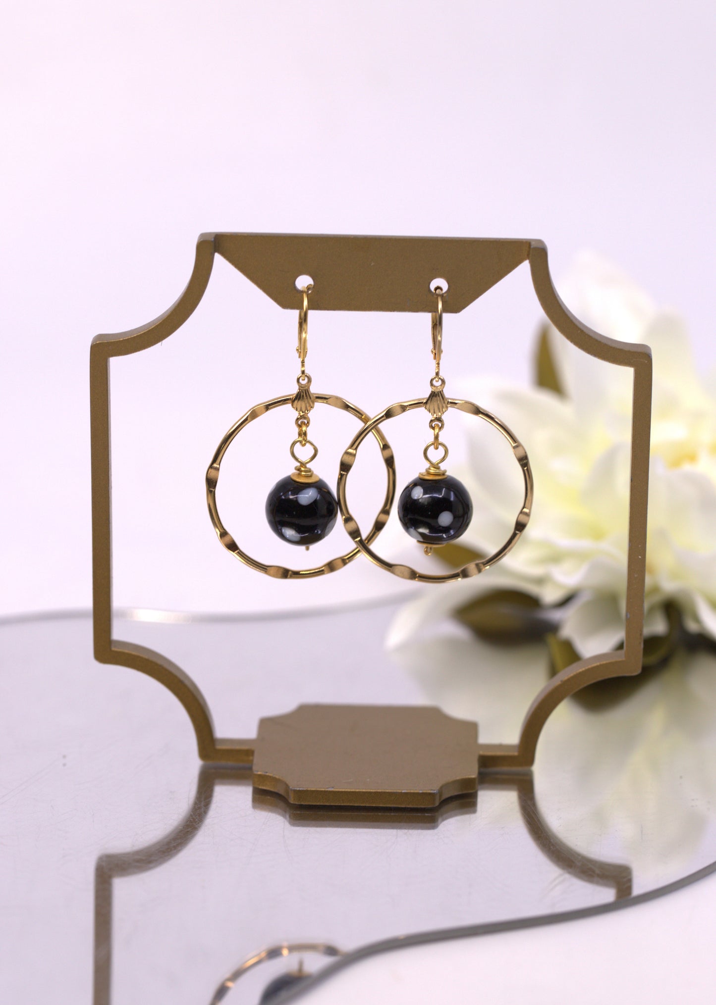 Gold hoop earrings with black beads on a decorative stand with flowers in the background