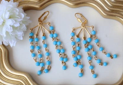 Gold and blue beaded earrings on a decorative white plate with a gold frame.