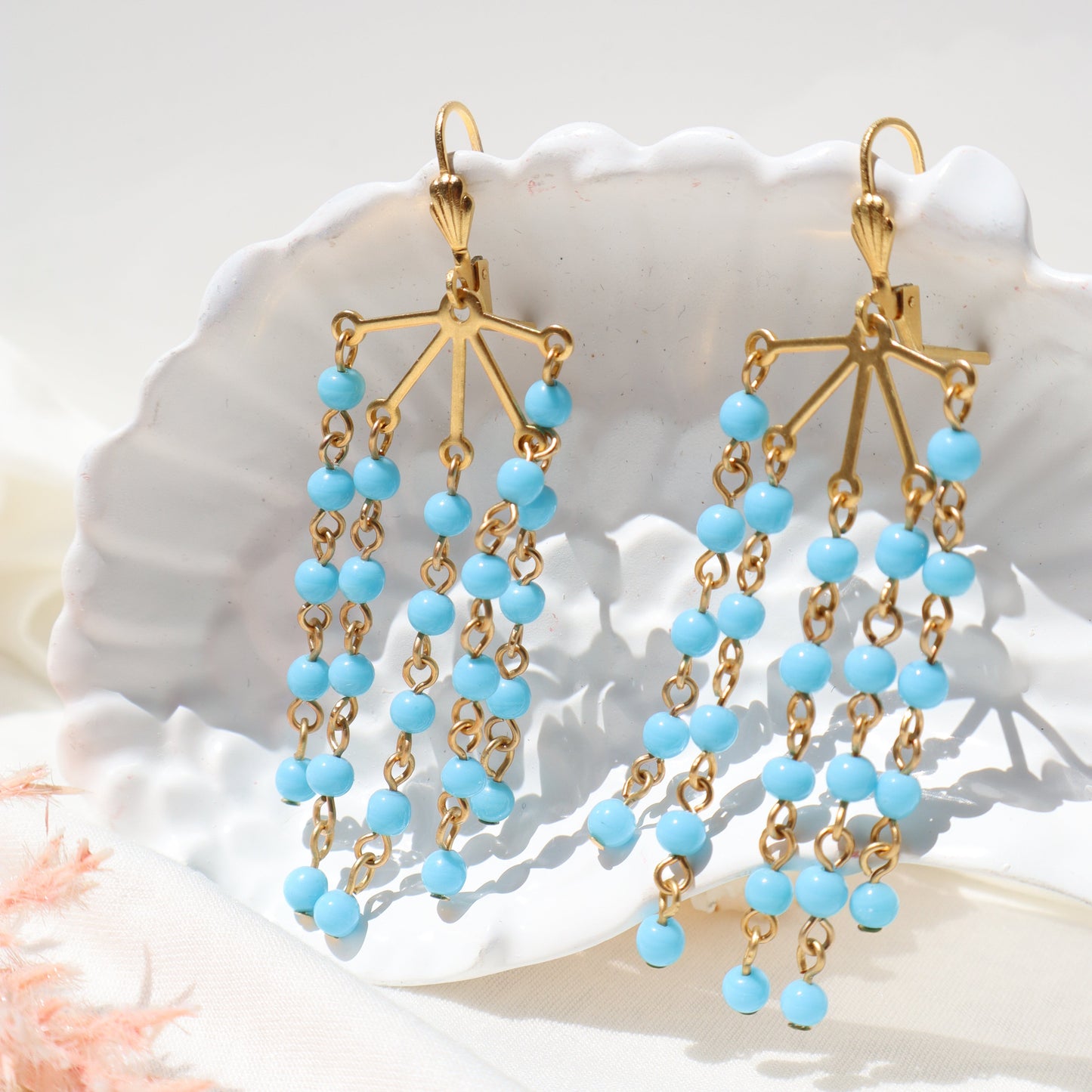 Gold and blue beaded earrings on a white shell background